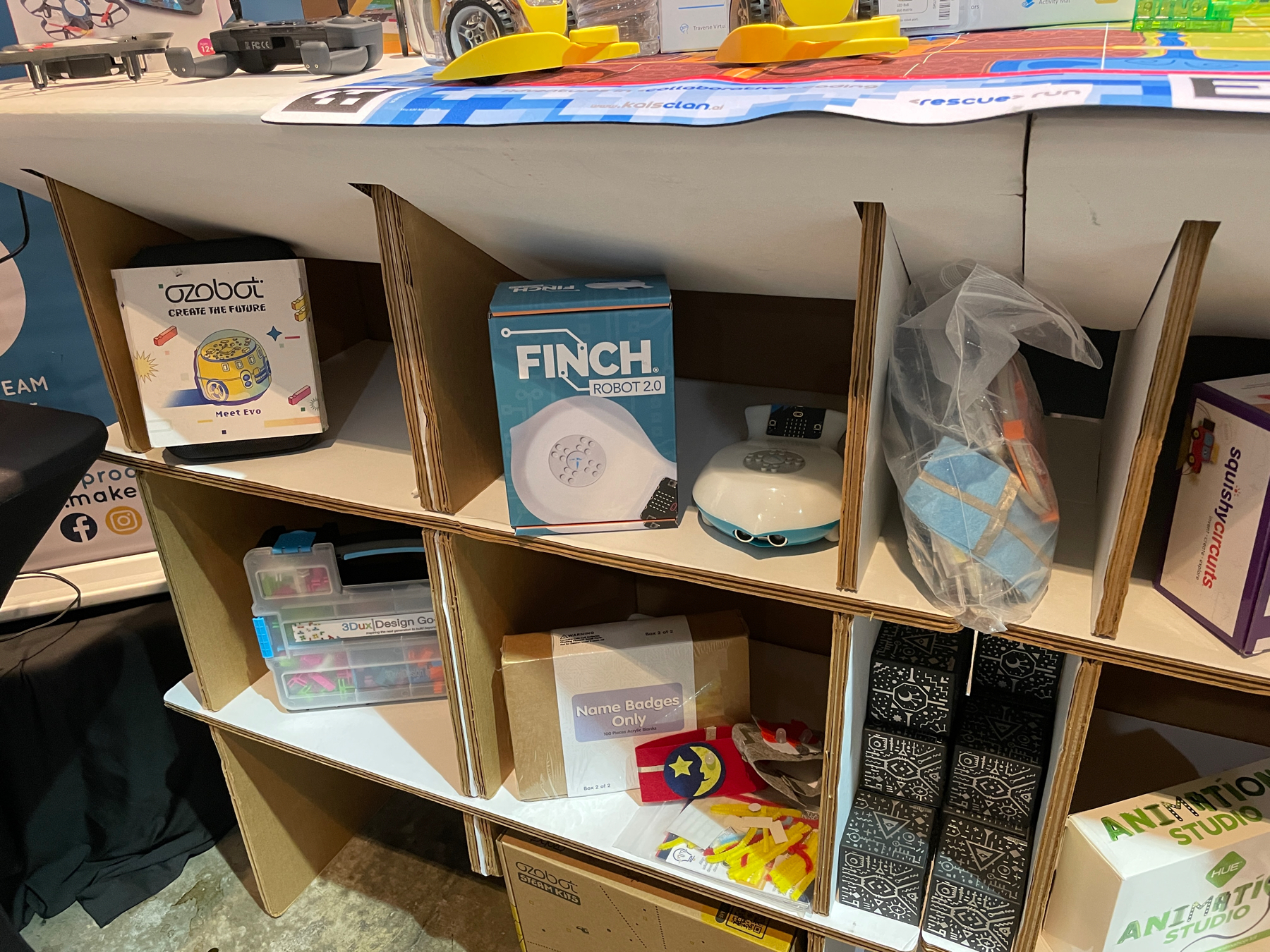 Auto-generated description: A display of various educational and robotic products, including Ozobot, Finch Robot 2.0, and other STEM-related items, is organized on shelves.