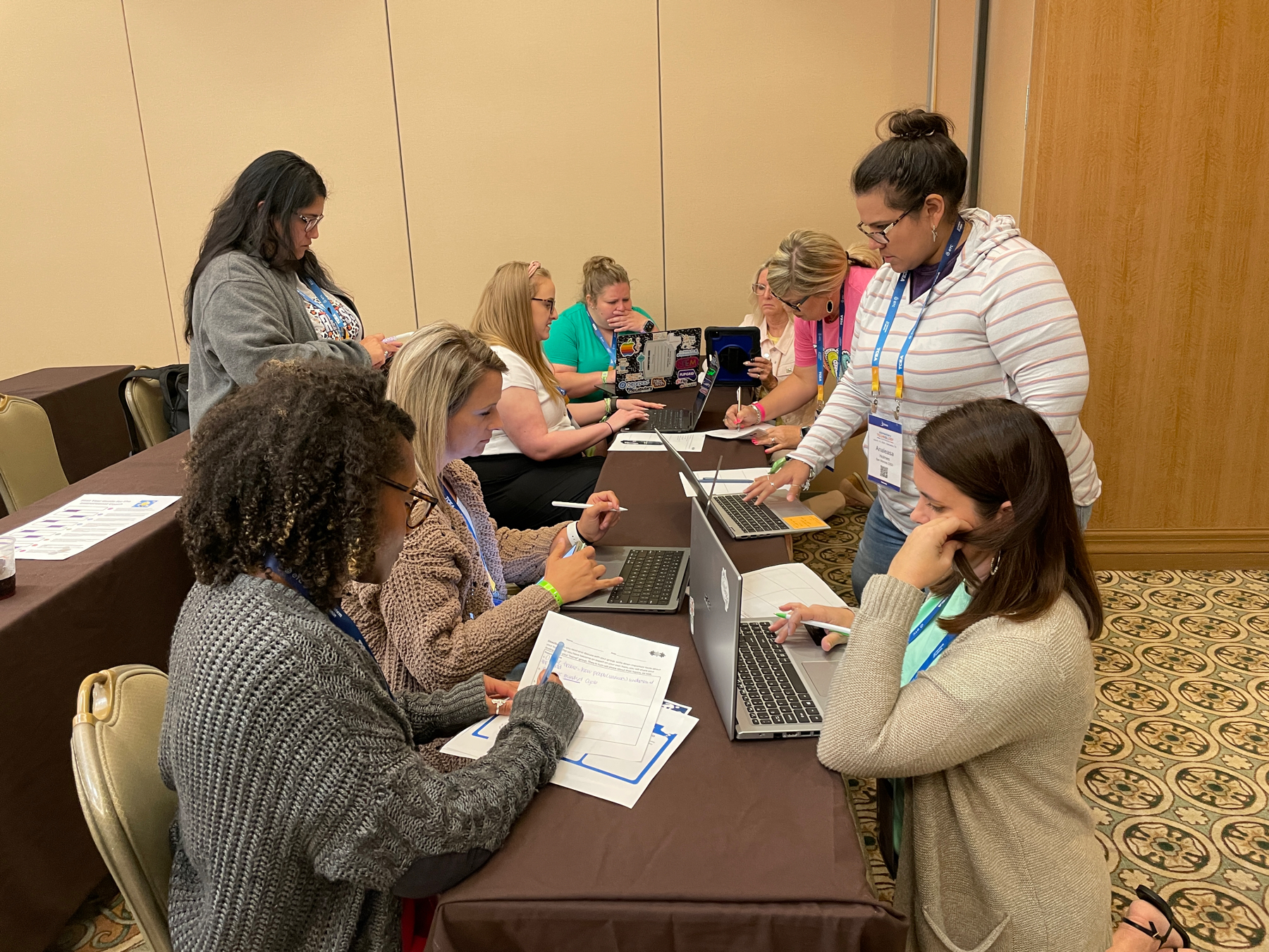 Auto-generated description: A group of people are collaborating and working on laptops around a conference table in a meeting room.