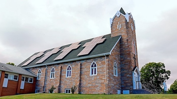 A brick church building with a tall tower features solar panels installed on its roof.
