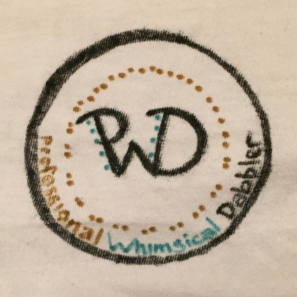 A logo written in marker on a section of white T-shirt features the stylized letters PWD encircled by dots and the words Professional Whimsical Dabbler.