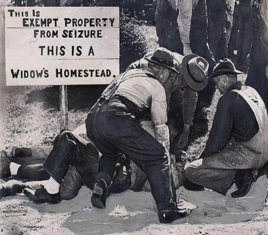 Auto-generated description: Several men stand over a person lying on the ground next to a sign that reads, THIS IS EXEMPT PROPERTY FROM SEIZURE. THIS IS A WIDOW'S HOMESTEAD.