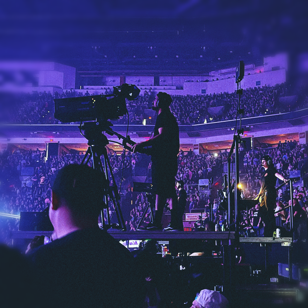 Cameraman and crew recording concert in a full stadium.