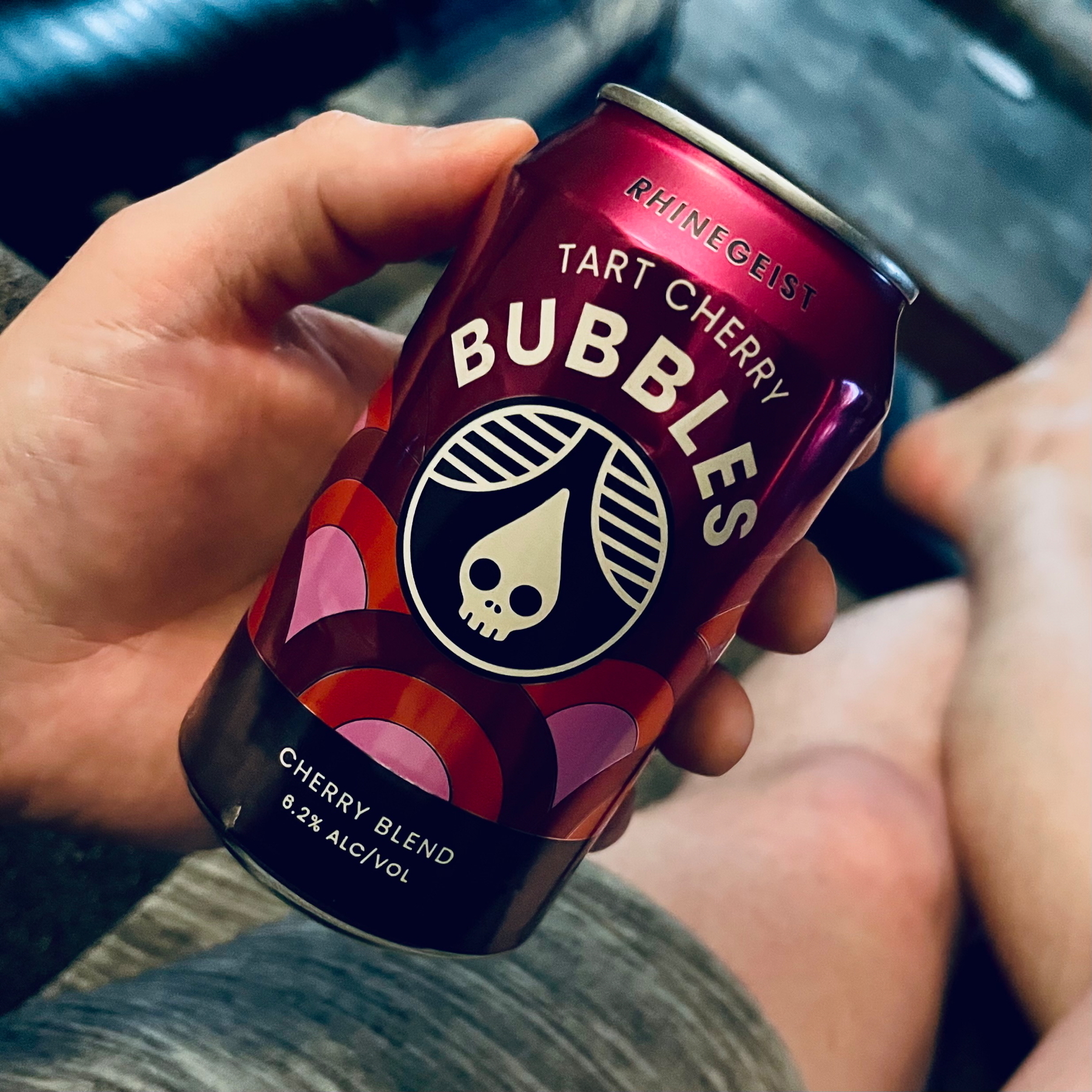 POV photo of me holding a can of Bubbles Tart Cherry from Rhinegeist. The can is different shades of red with pink accents and has the company’s skull logo in the center. It says “Cherry Blend, 6.2% alcohol”