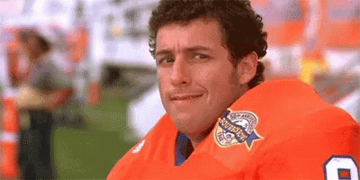 Bobby Boucher in The Waterboy. He's in an orange jersey is making an awkward facial expression and looking off screen. 