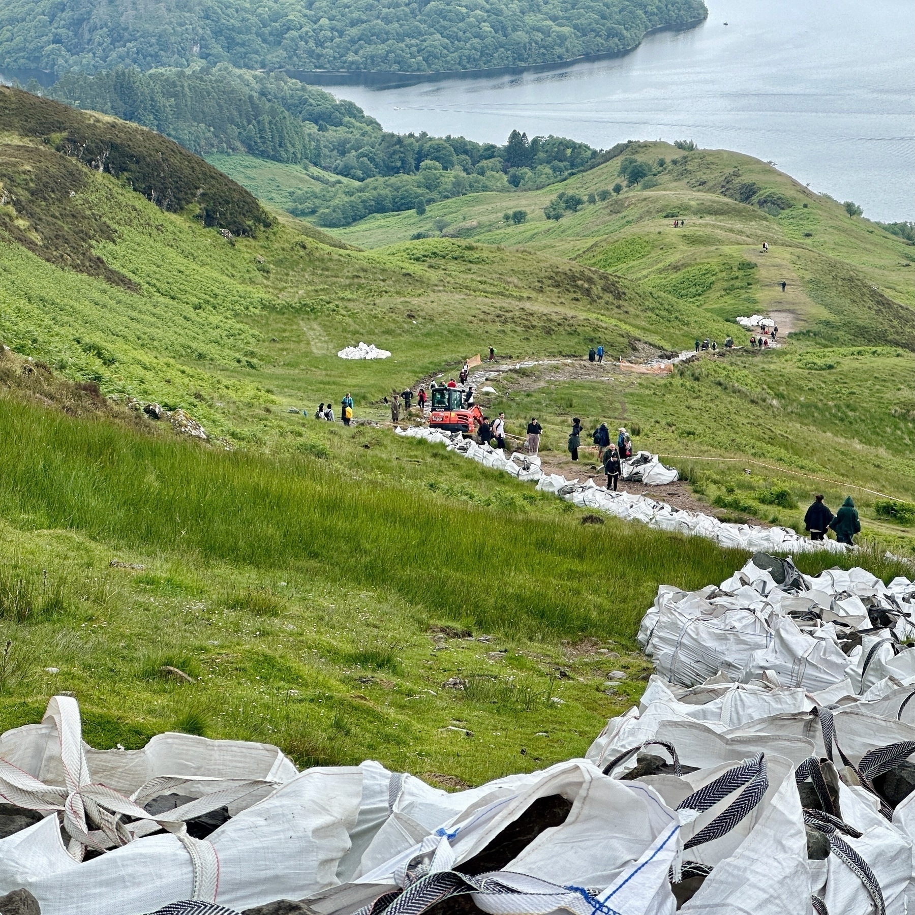 A digging machine is parked about half way up the side of the hill, with lots of bags of rocks visible.