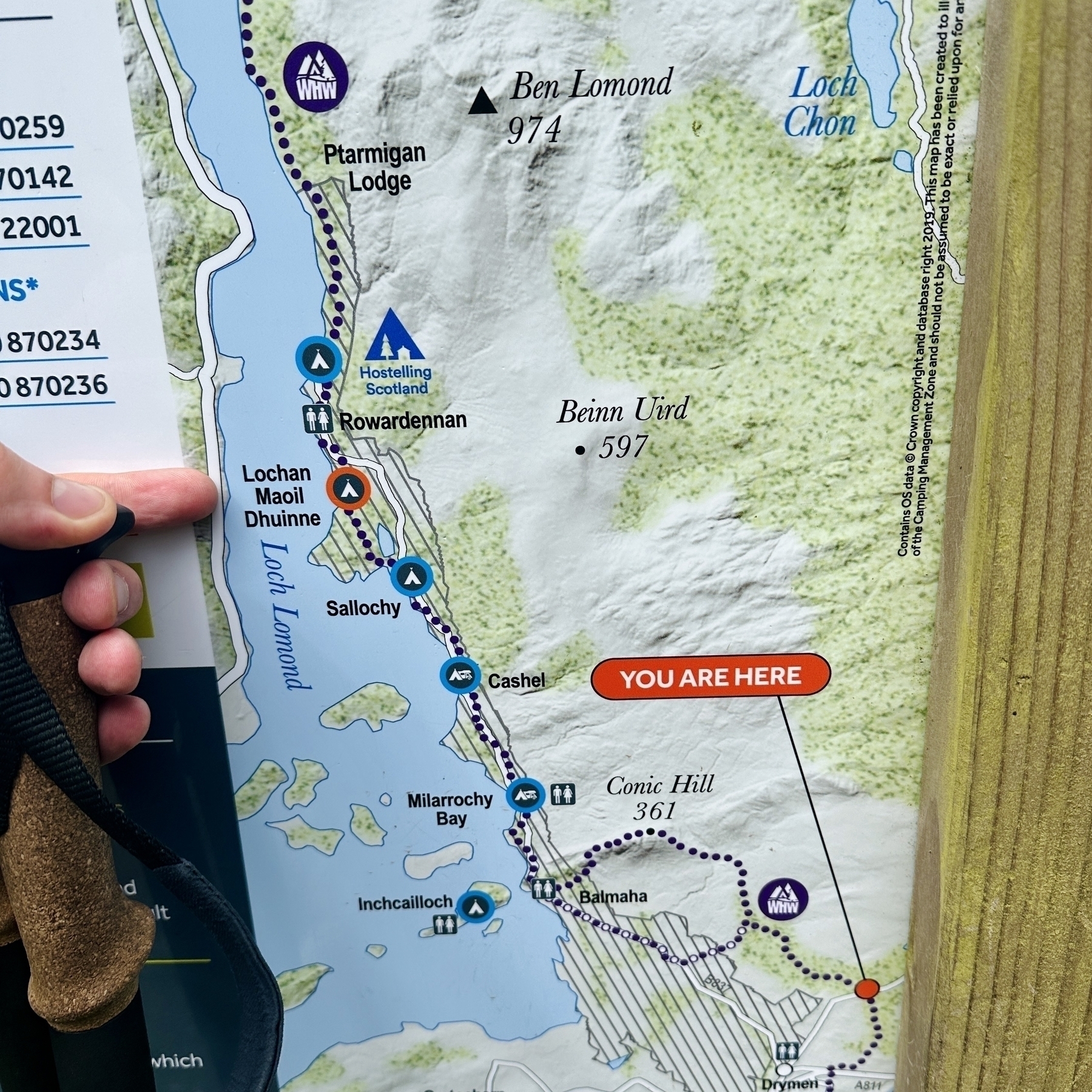 A map shows the starting point of the day whilst I point to my intended destination, Lochan Maoil Dhuinne, a permitted wild camp spot on the shores of Loch Lomond.