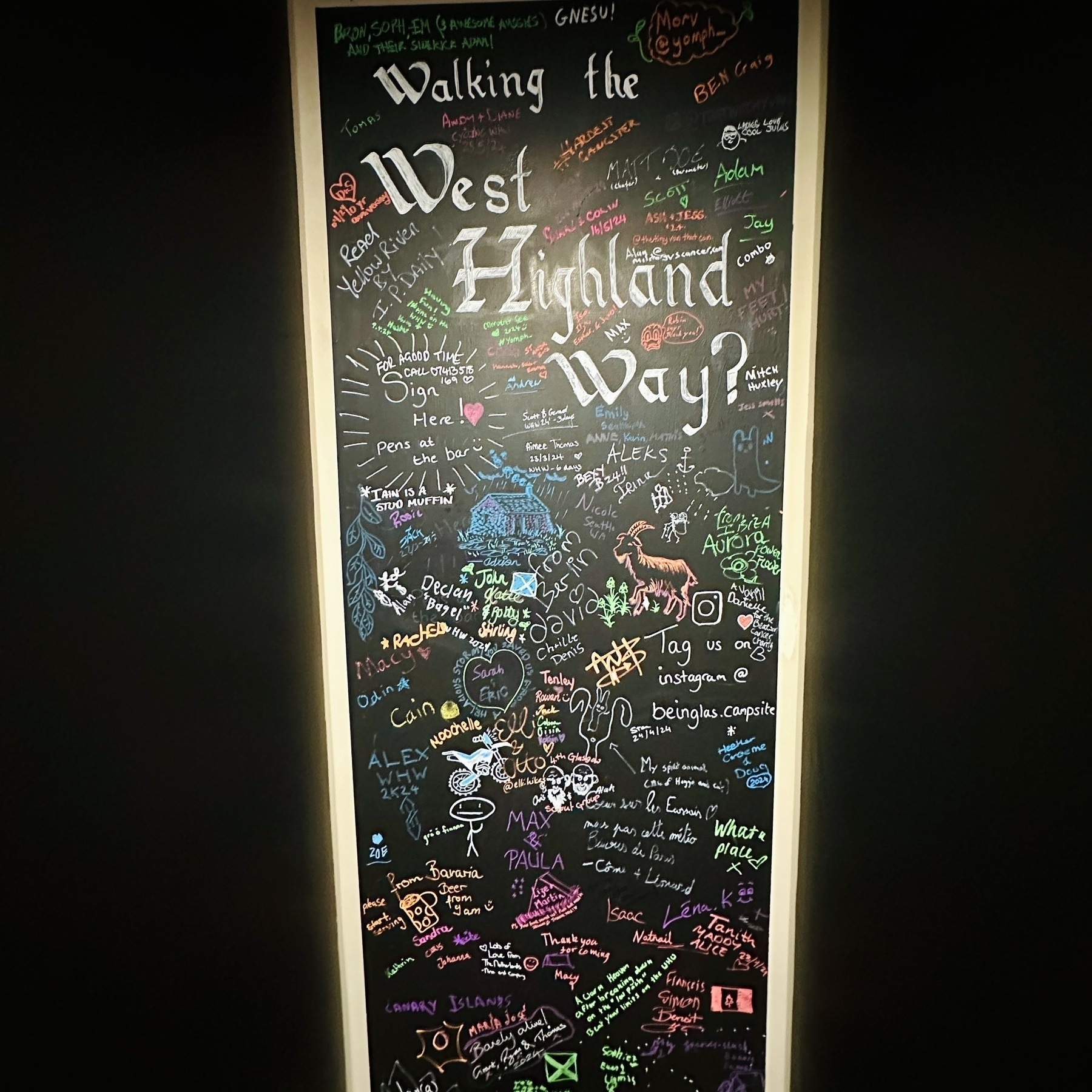 Auto-generated description: A blackboard filled with colorful drawings, messages, and signatures commemorates walking the West Highland Way.