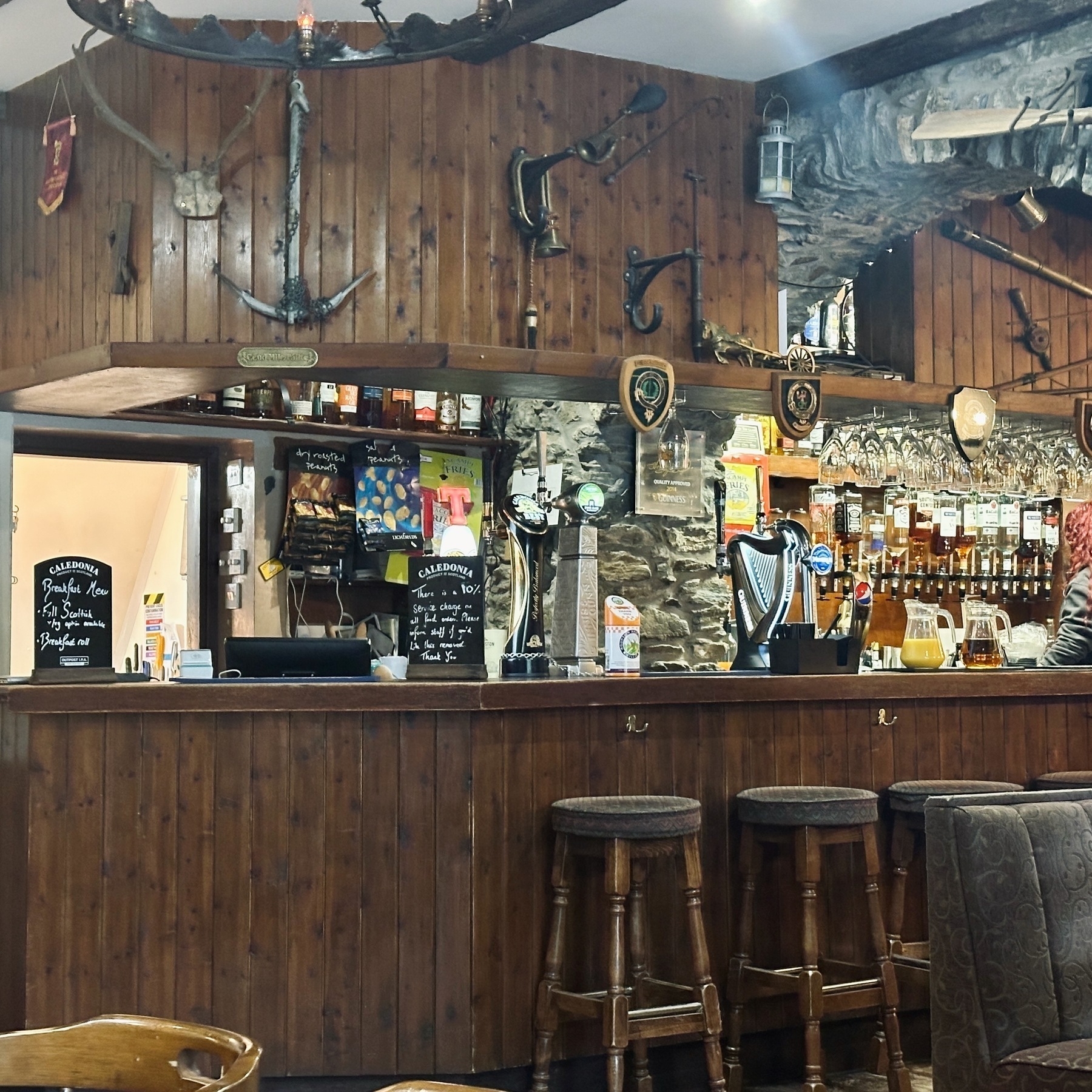 Auto-generated description: A rustic bar interior is adorned with wooden panels, hunting trophies, and various bottles, with bar stools placed in front of the counter.