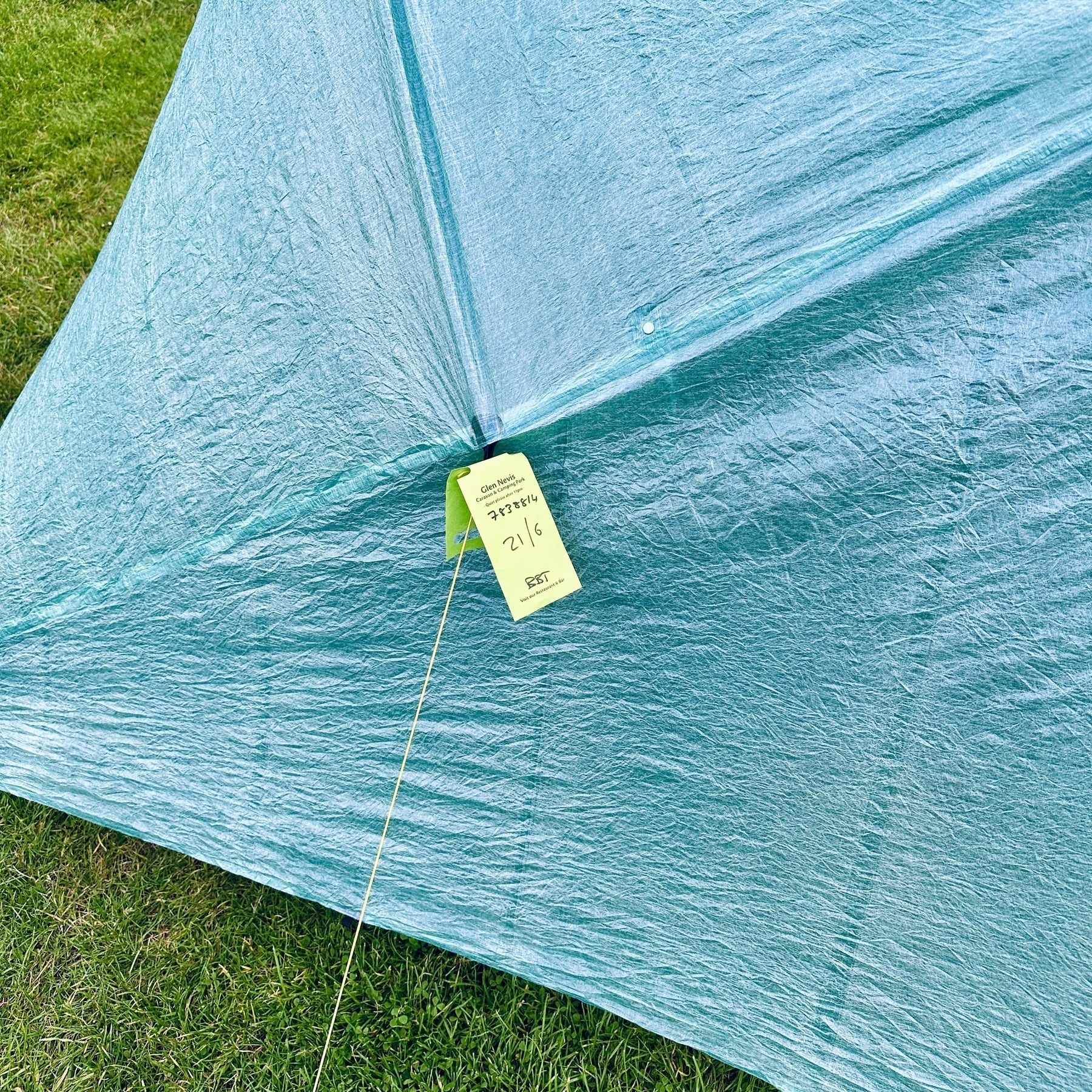 Auto-generated description: A blue tent is set up on a grassy field, with a green ticket labeled Glen Nevis camping park attached to it.