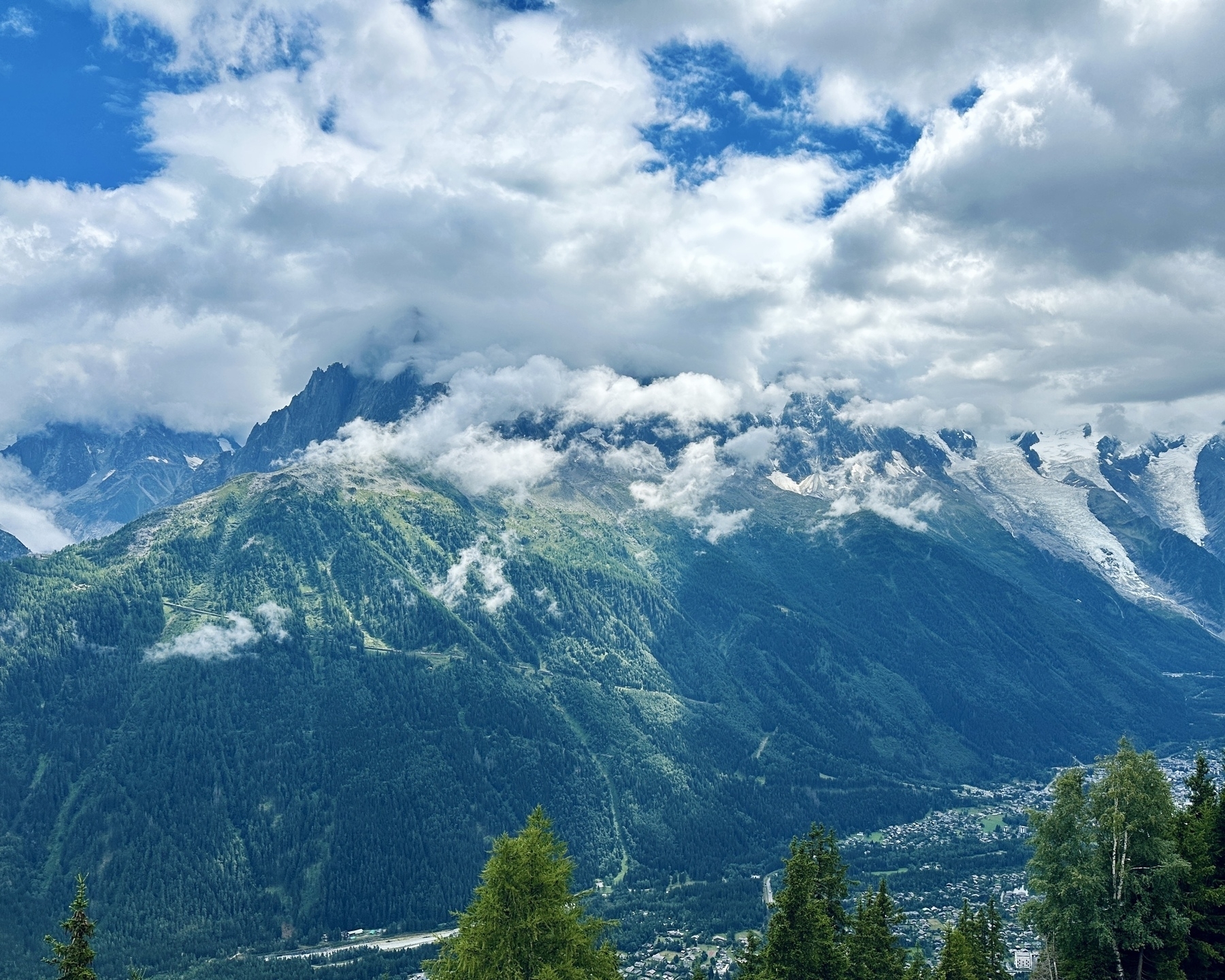 Auto-generated description: A picturesque mountain range is partially shrouded in clouds, with lush green forests and a valley below.