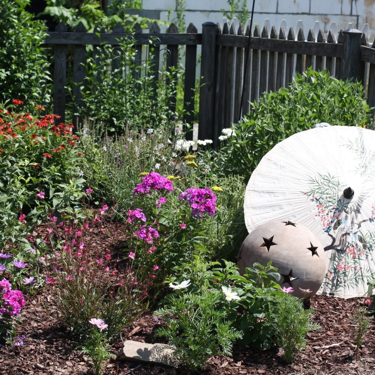 Auto-generated description: A garden features vibrant flowers, lush greenery, and a decorative white parasol with a painted design.