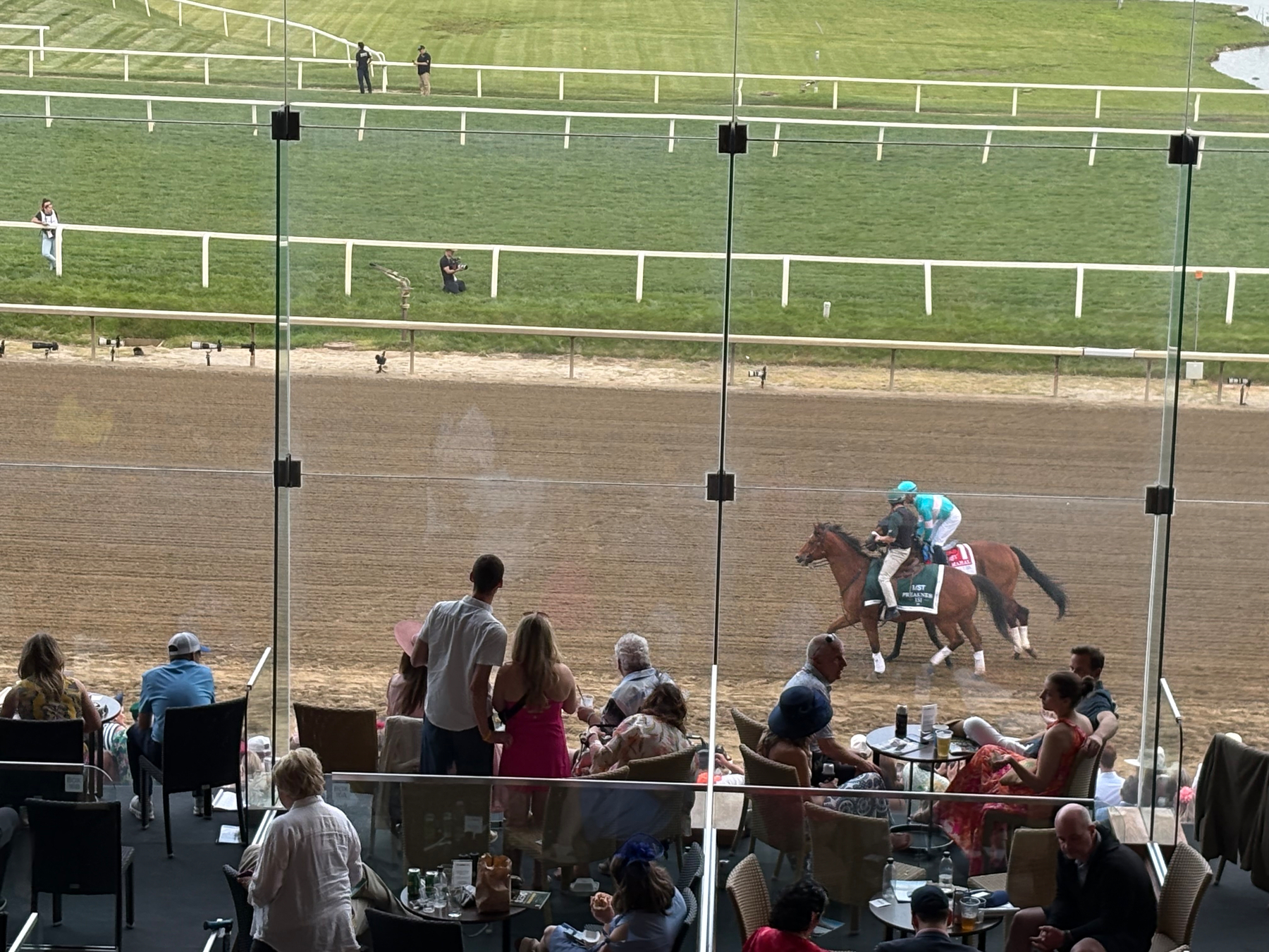 Auto-generated description: Spectators seated at tables behind glass are watching a horse race on a dirt track.