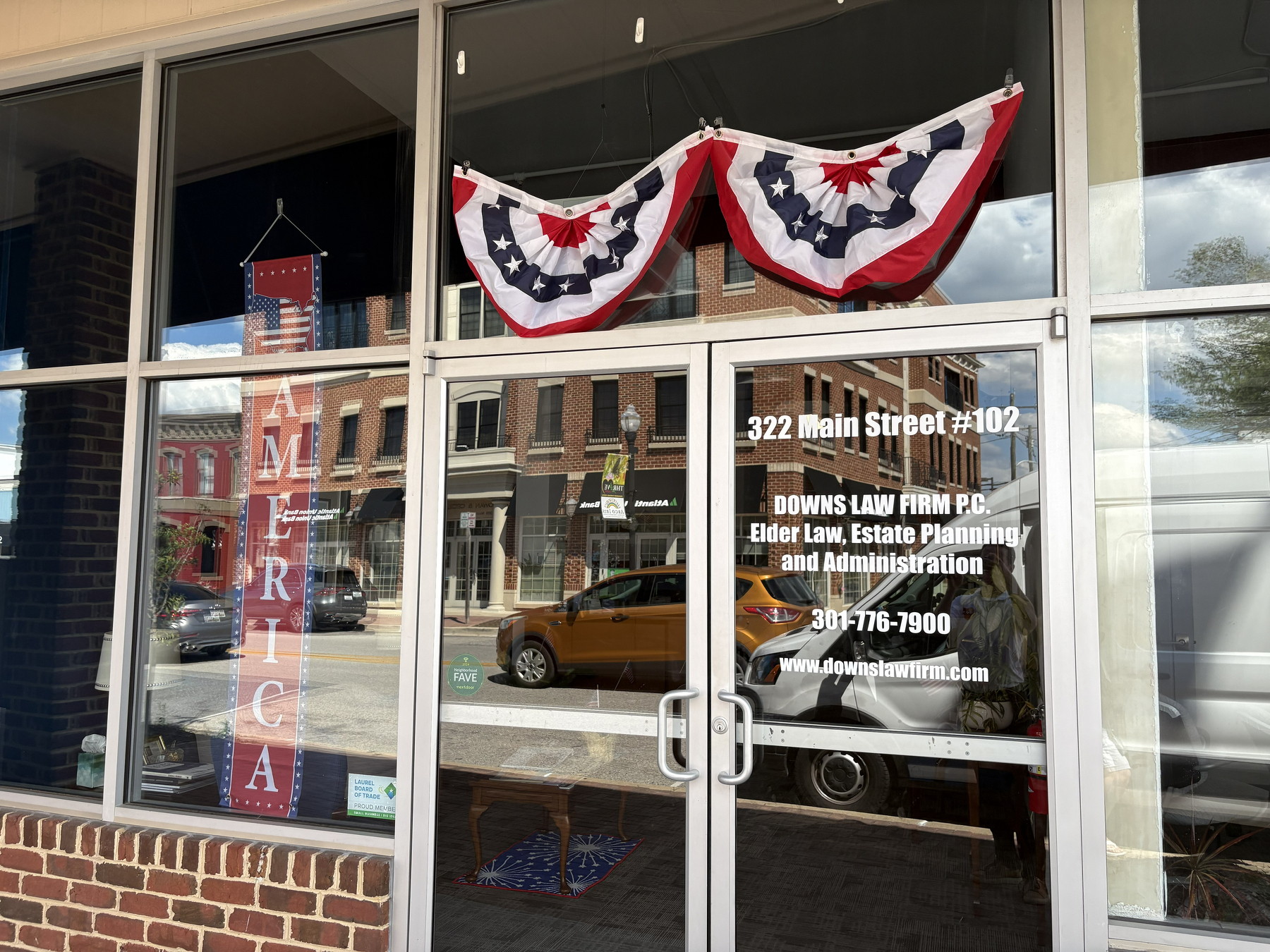 Auto-generated description: A storefront window displays patriotic decorations and signage for Downs Law Firm P.C., specializing in elder law, estate planning, and administration.