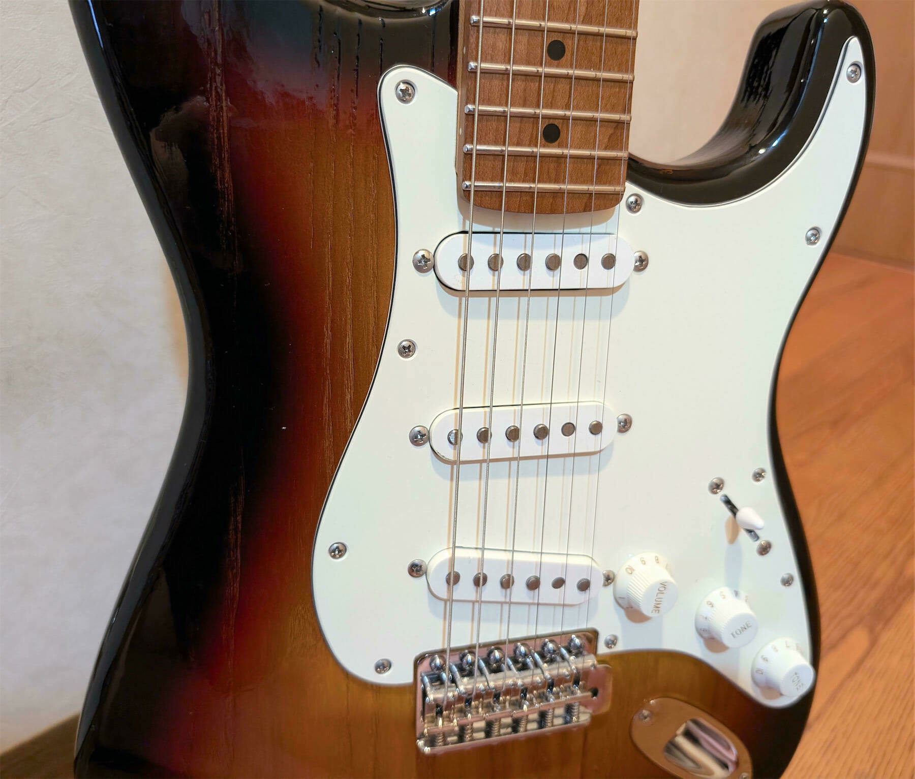 A close-up of a sunburst electric guitar with a white pickguard and three single-coil pickups is shown.