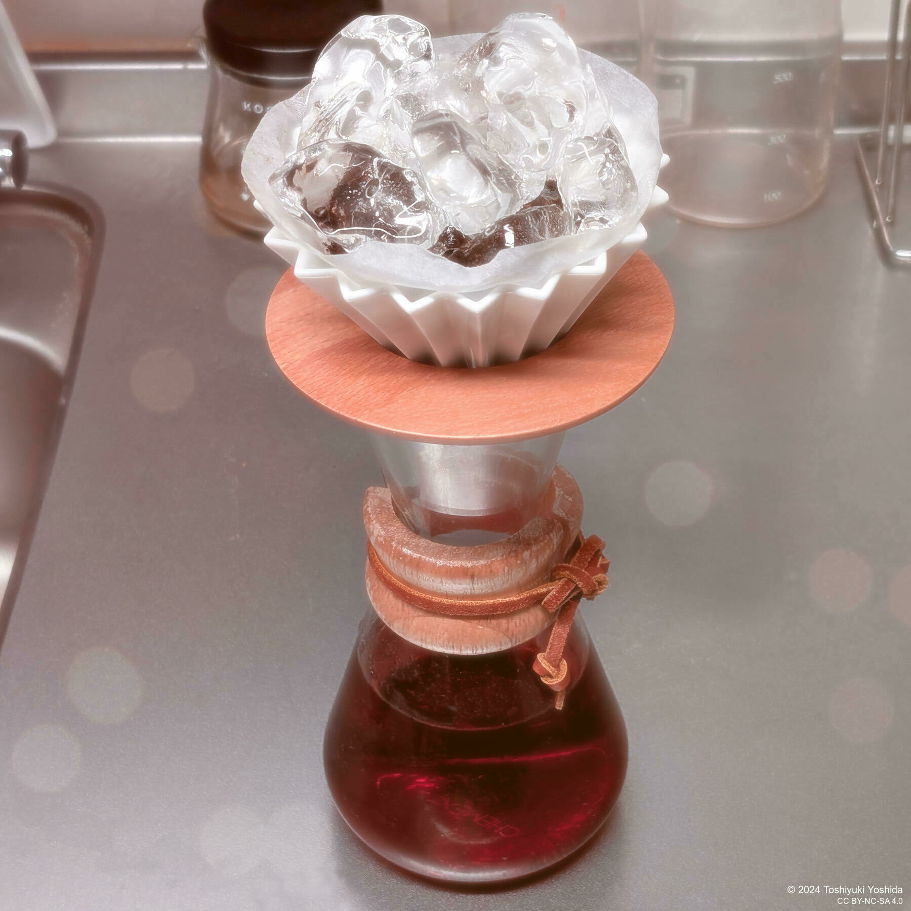 A coffee brewing setup features a Chemex with ice cubes in a filter placed on top.