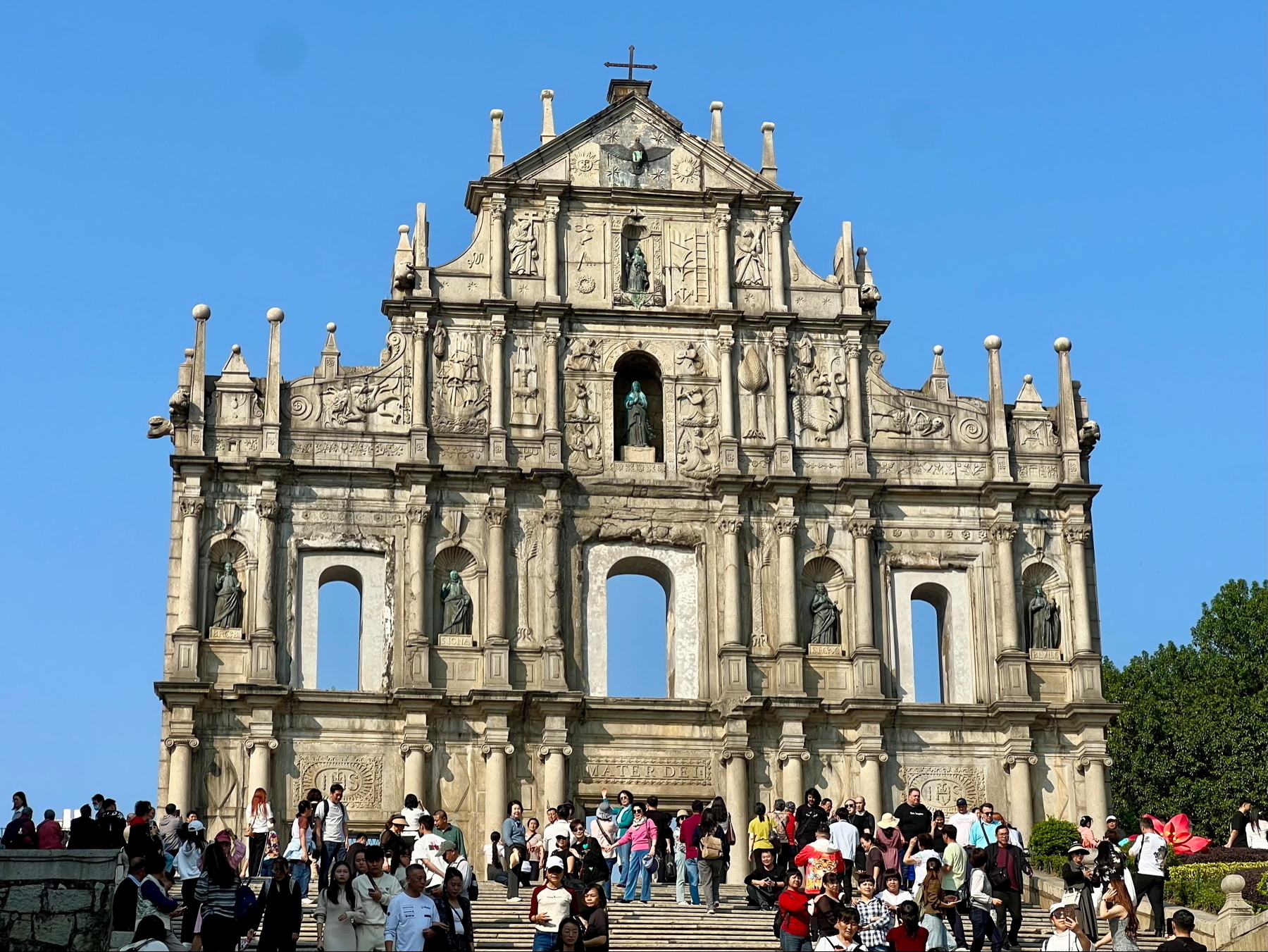 Auto-generated description: A large crowd gathers in front of the historic ruins of St. Paul's in Macau, featuring its grand stone facade and ornate architectural details.