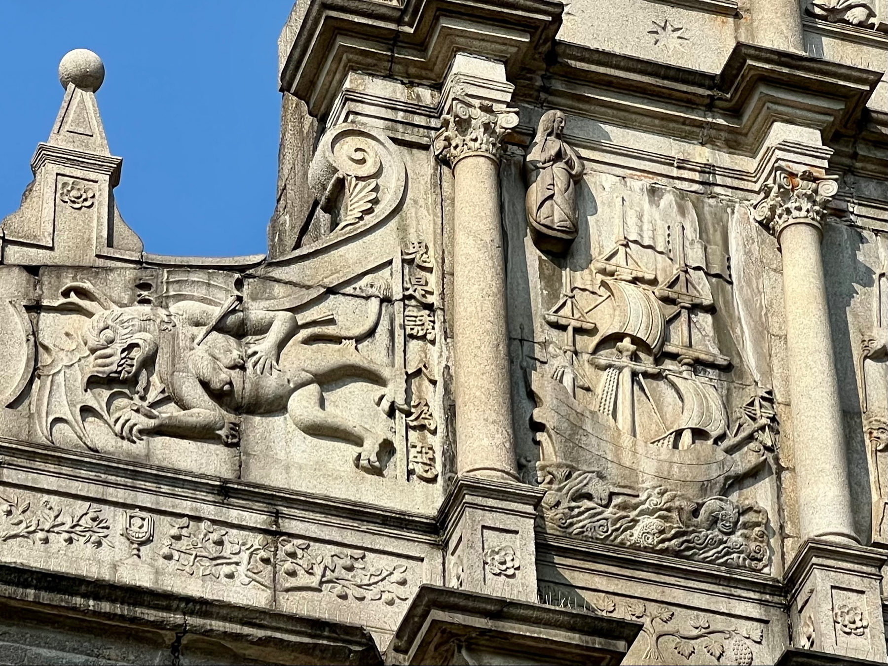 Auto-generated description: A detailed stone carving on a building facade features a dragon-like creature and a ship.