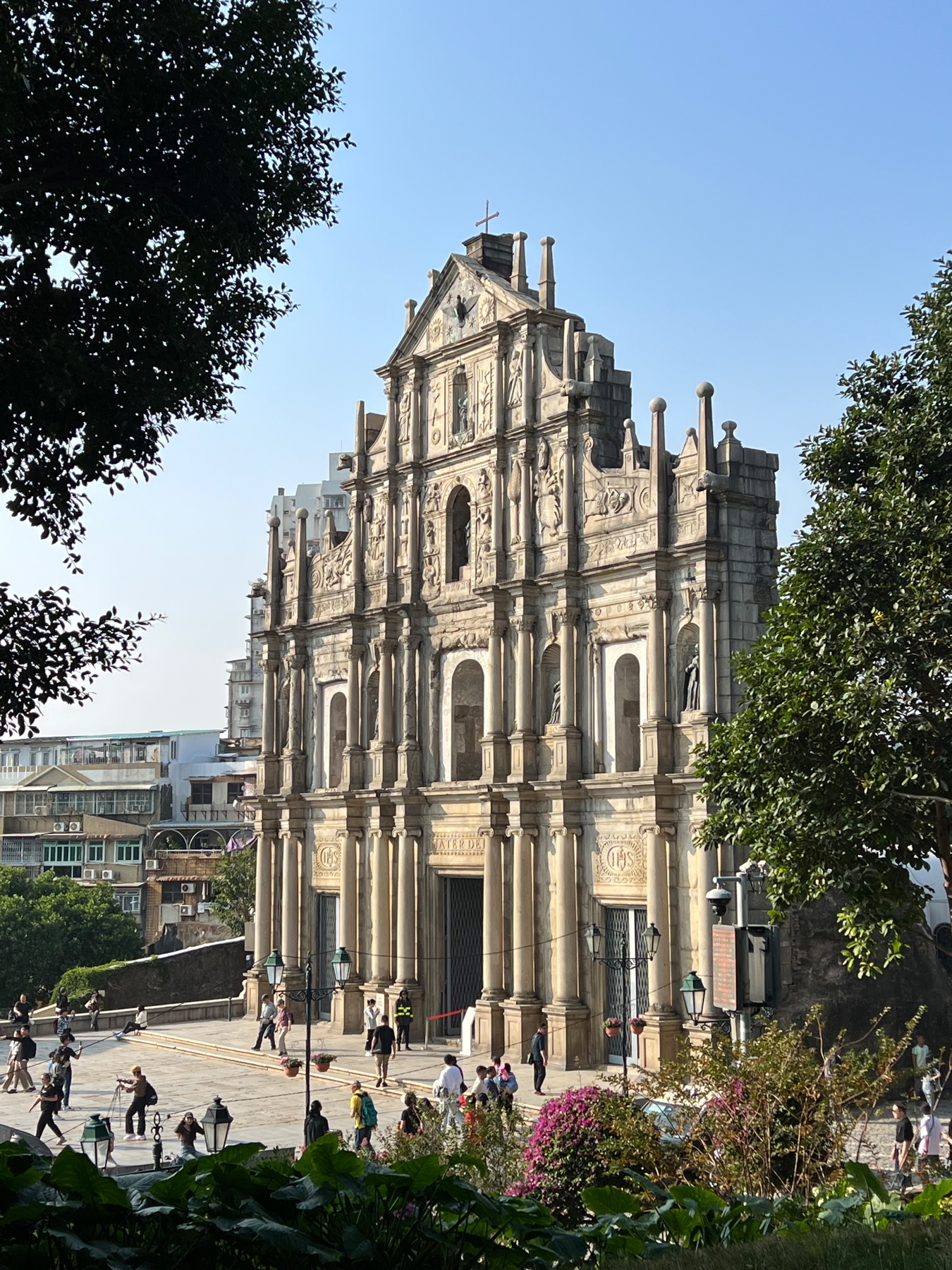 Auto-generated description: The image shows the ruins of St. Paul's in Macau, with its intricate stone facade surrounded by trees and visitors.