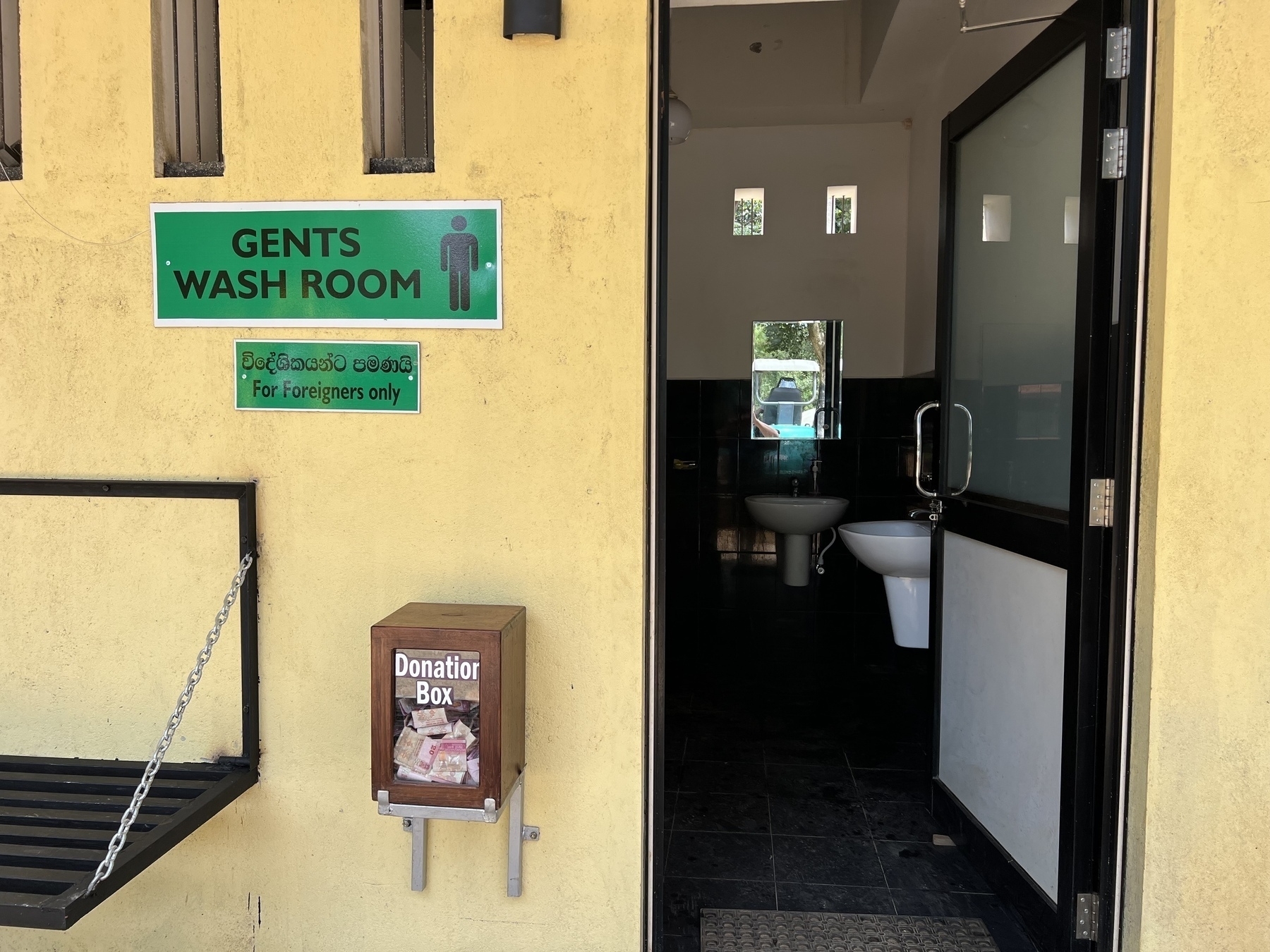 A men's restroom entrance is shown with a sign indicating it is for foreigners only and a donation box nearby.