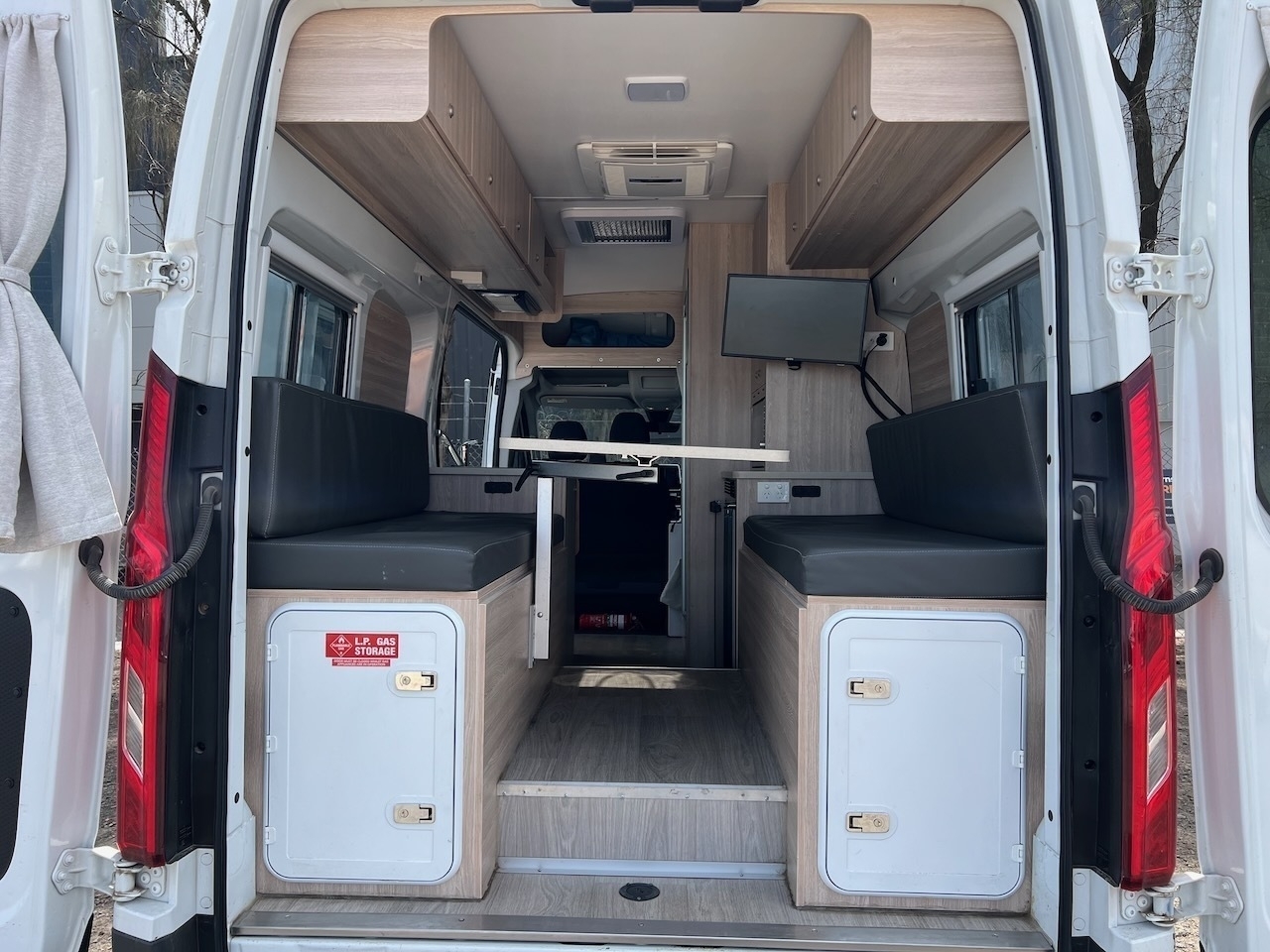 Auto-generated description: A camper van with a modern interior features two seating areas, a mounted TV, storage compartments, and an extendable table.