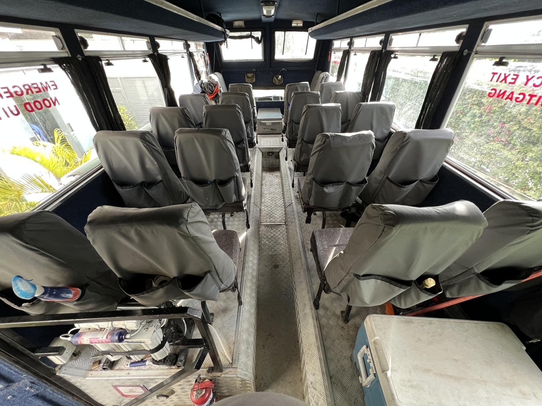 Auto-generated description: A bus interior showing rows of empty, gray-covered seats and windows with emergency exit signs.