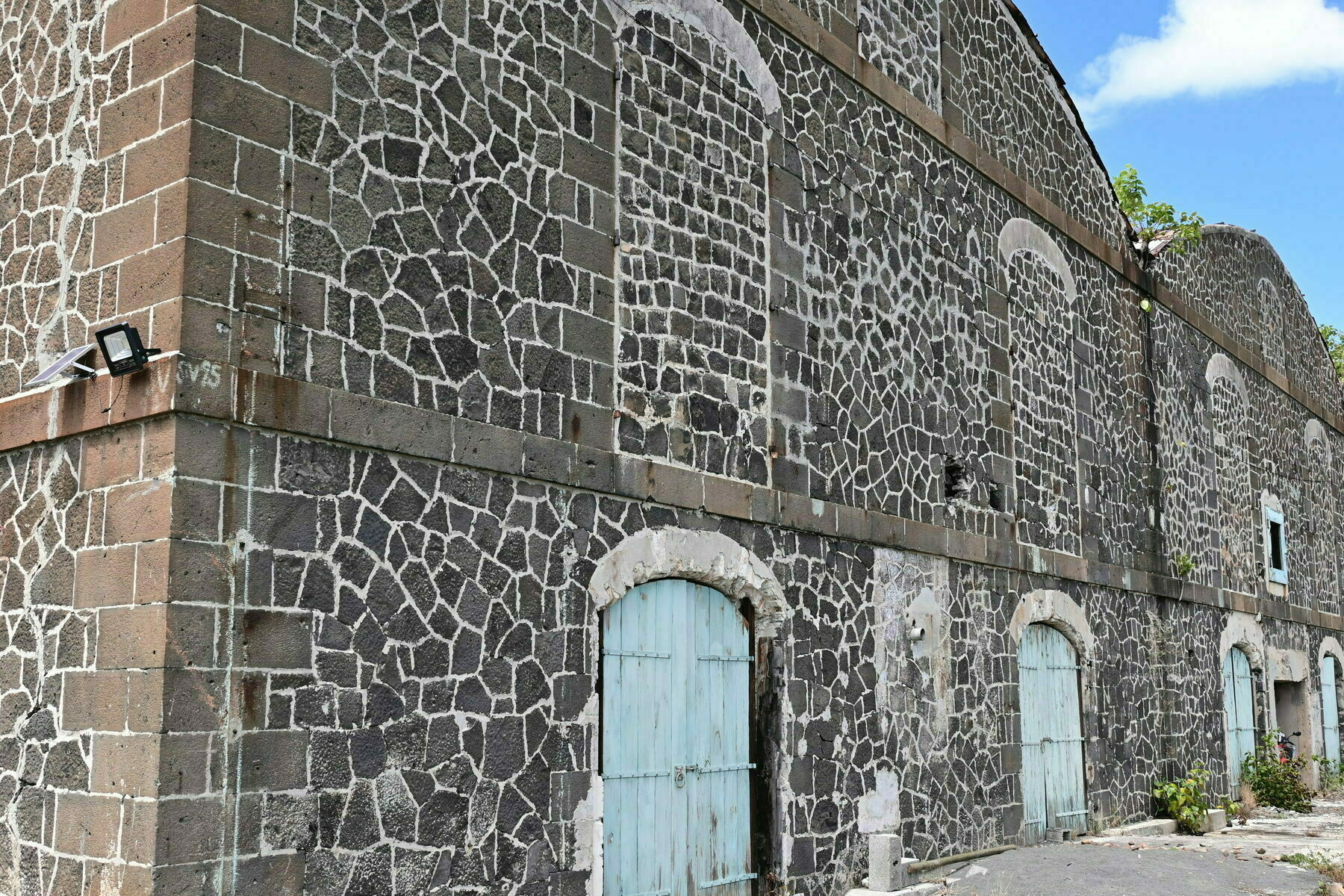 Auto-generated description: A stone building with arched windows and blue wooden doors stands against a clear sky.