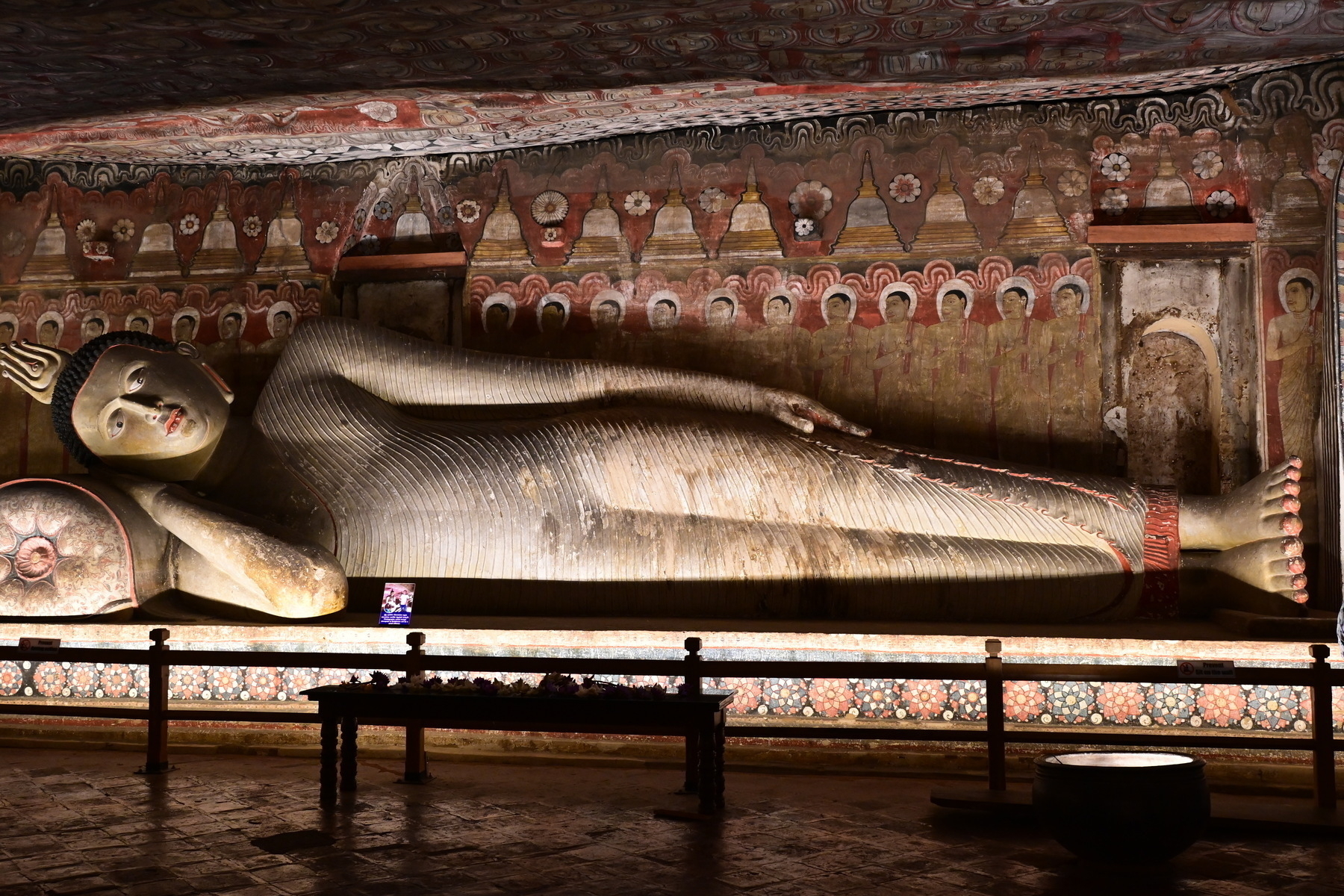 Auto-generated description: A large, reclining Buddha statue is displayed indoors, surrounded by intricately painted walls and a decorated ceiling.