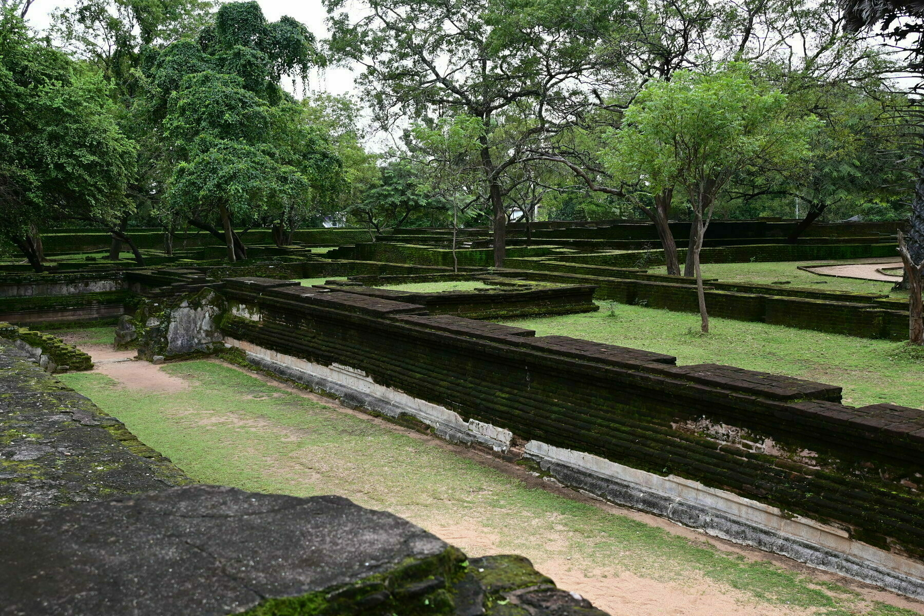 Auto-generated description: Ancient stone walls and pathways are surrounded by lush greenery and trees in a historical park or garden.