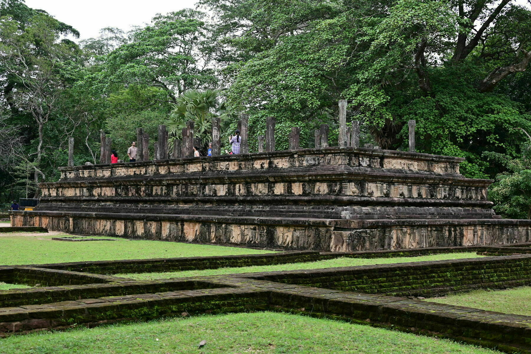 Auto-generated description: An ancient stone structure, surrounded by lush greenery, features a series of vertical pillars on a raised platform.