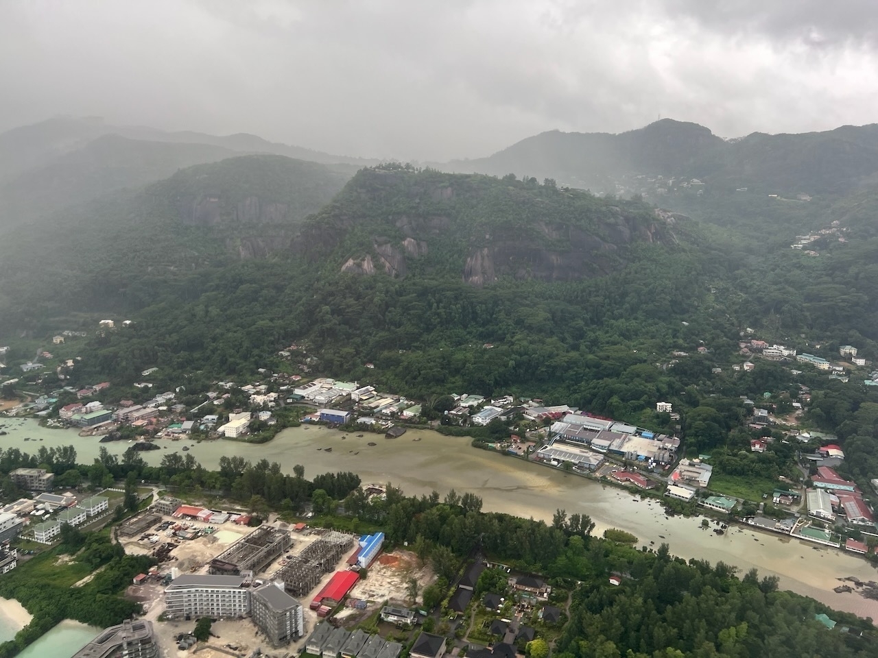 Auto-generated description: An aerial view showcases a lush, mountainous landscape with buildings scattered across a valley, under overcast skies.