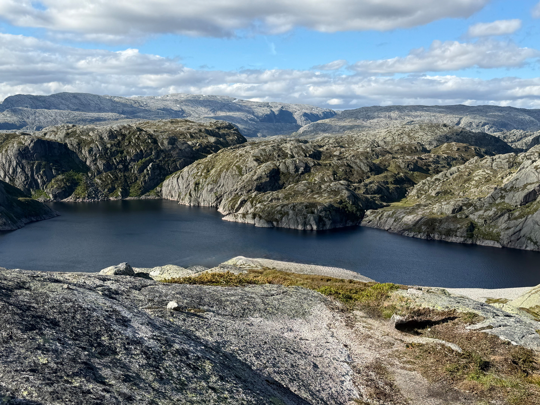 A serene lake is surrounded by rugged rocky hills under a partly cloudy sky.