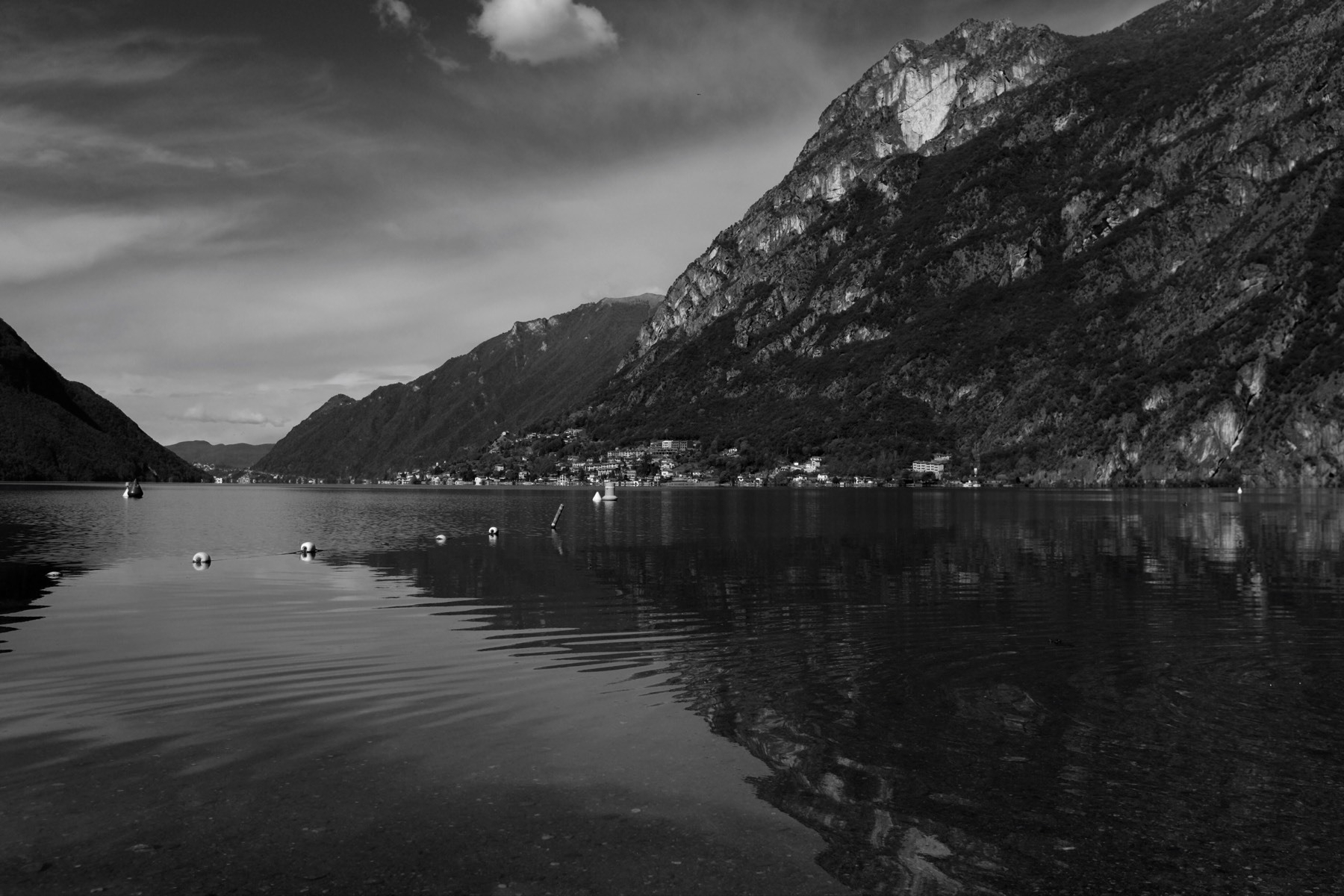 Black-and-white landscape photo of Lake Lugano with mountains and village in the background