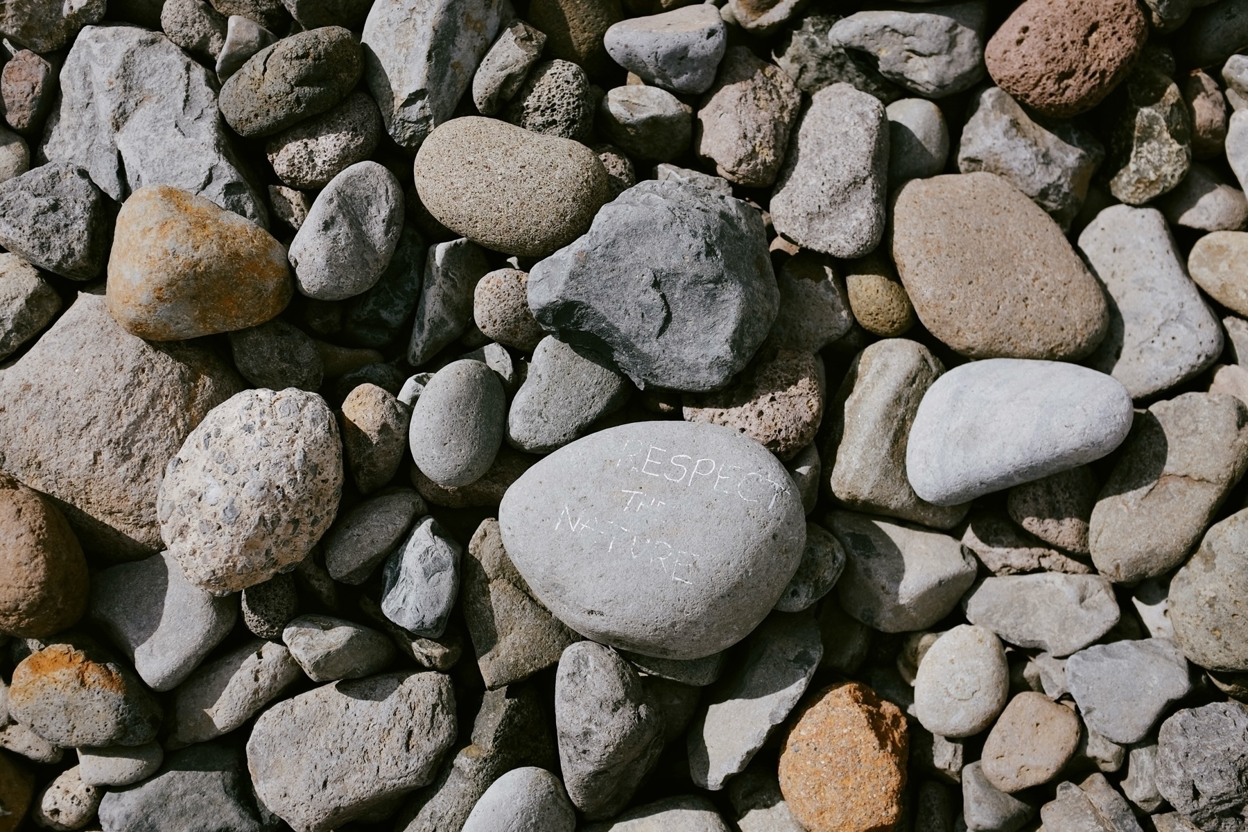 A collection of variously sized stones, with one in the center engraved with the words “RESPECT THE NATURE.