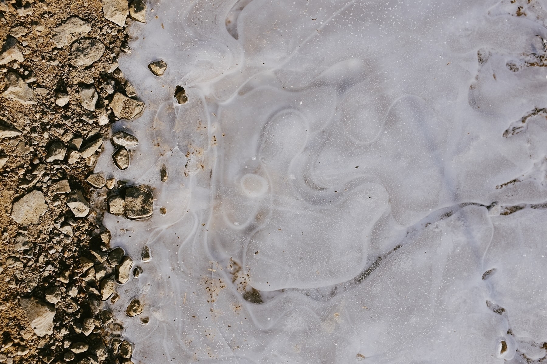 Rocks lie along the edge of a smooth, icy surface with swirling patterns.