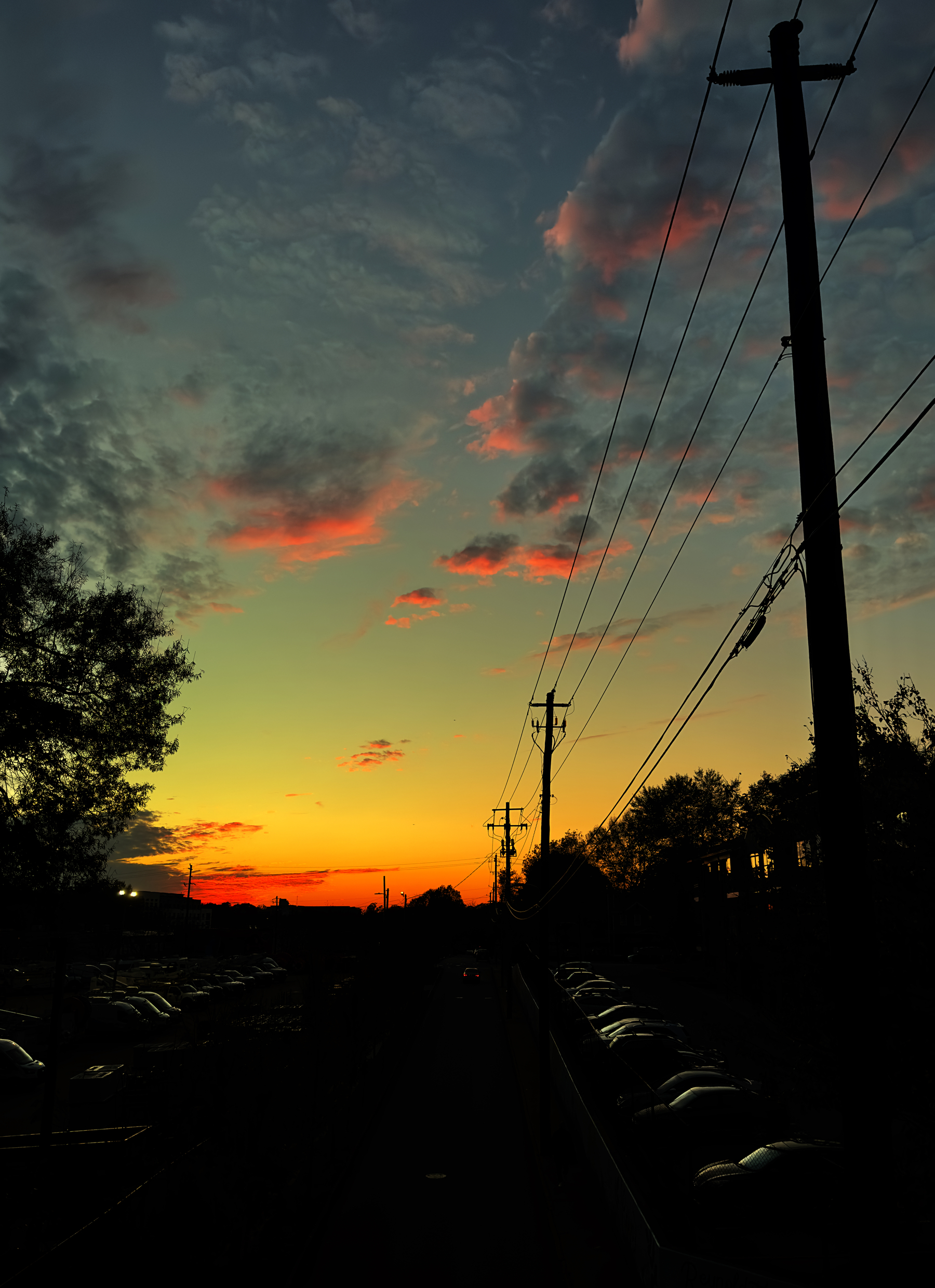 A view of a street from above, lined with telephone poles leading toward the evening sky filled with afterglow. 