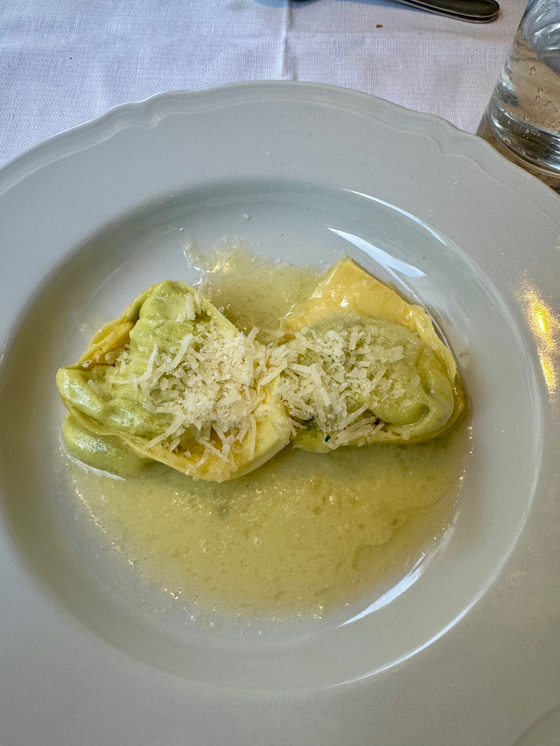 A plate of green and yellow tortelloni with grated cheese on top, served with light sauce on a white plate.
