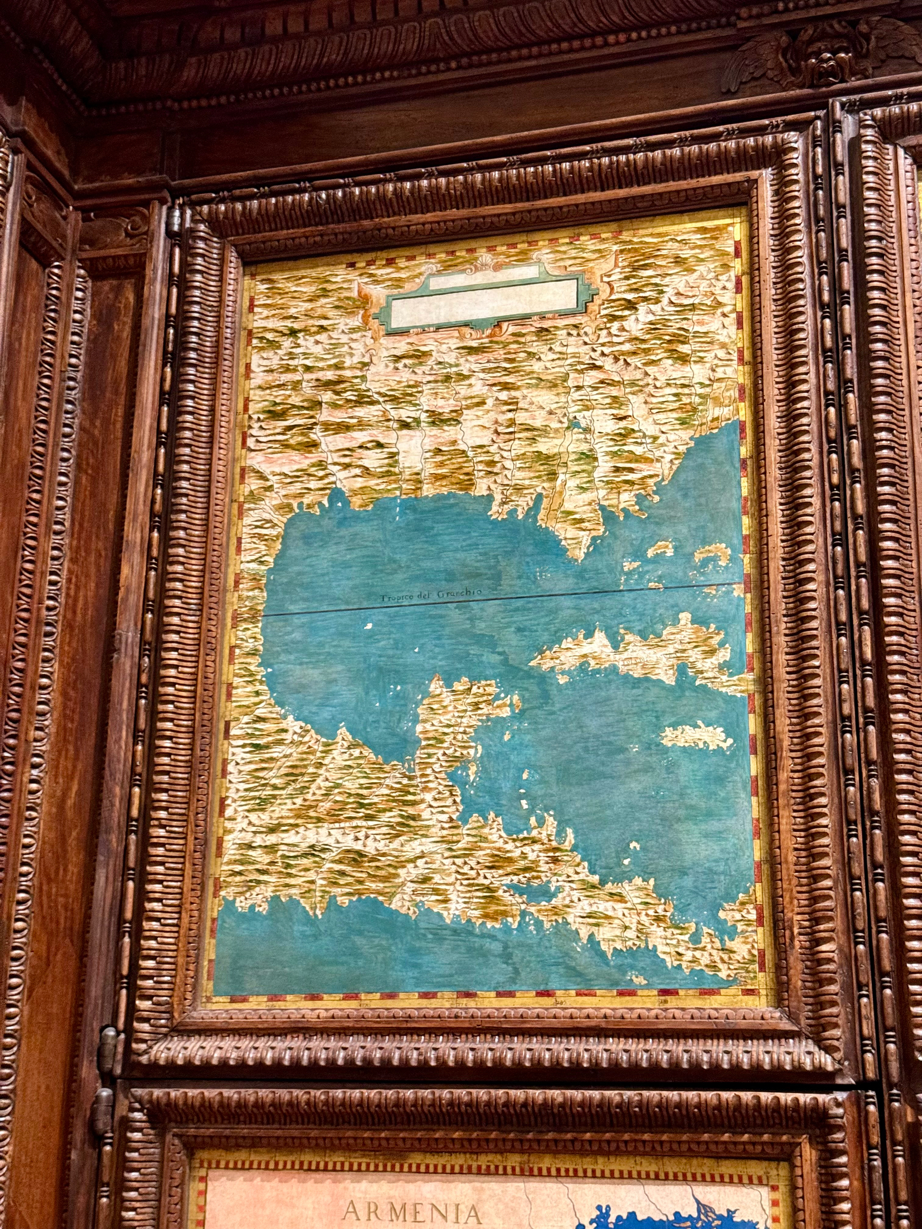 An old, framed map with an ornate wooden border showing a coastal region. The map is primarily in blue and gold with visible terrain details. The body of water is extensive with some islands scattered.