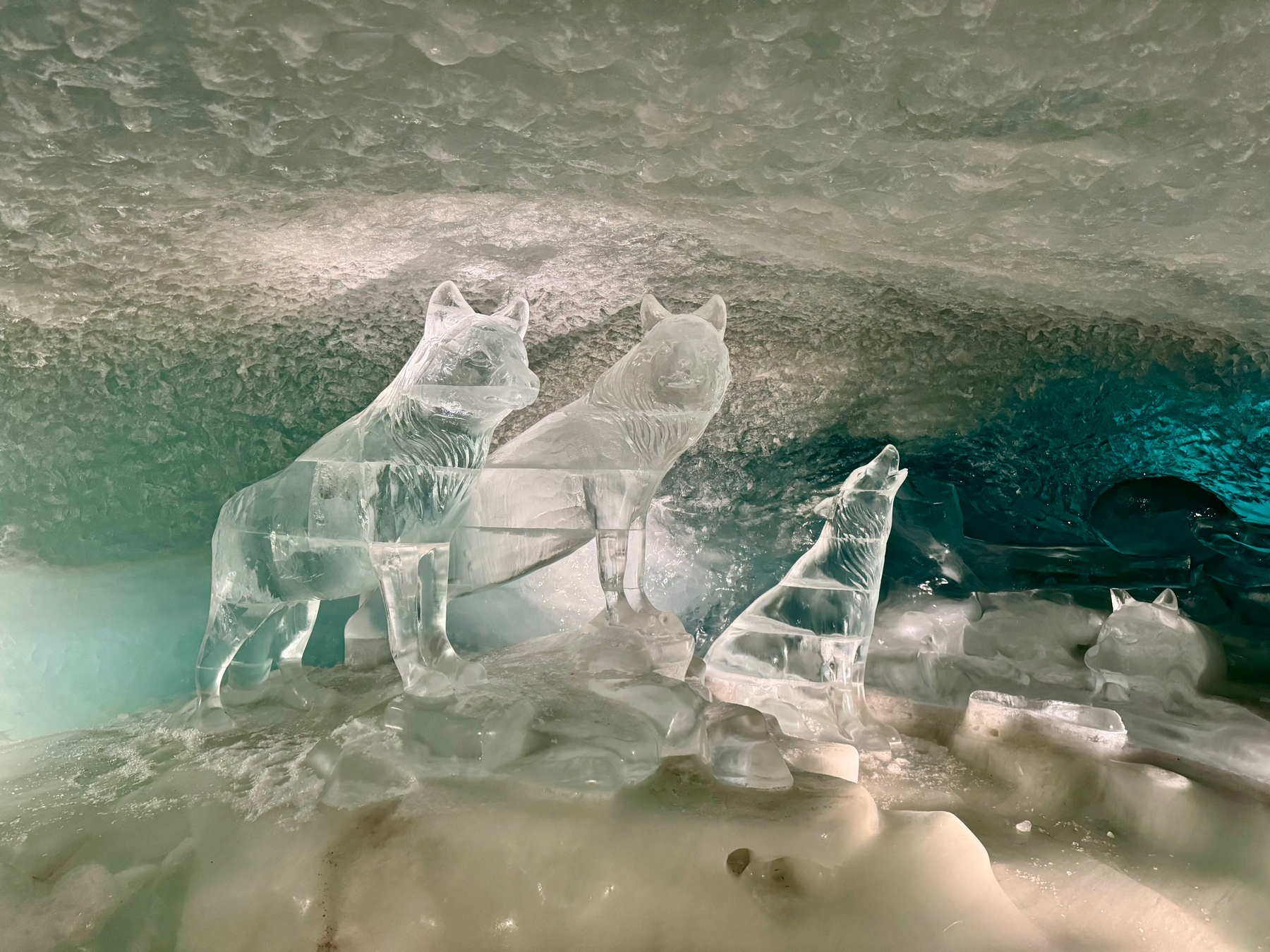 Ice sculptures of wolves displayed in a cave-like setting with icy textures and a blue-green ambient light.