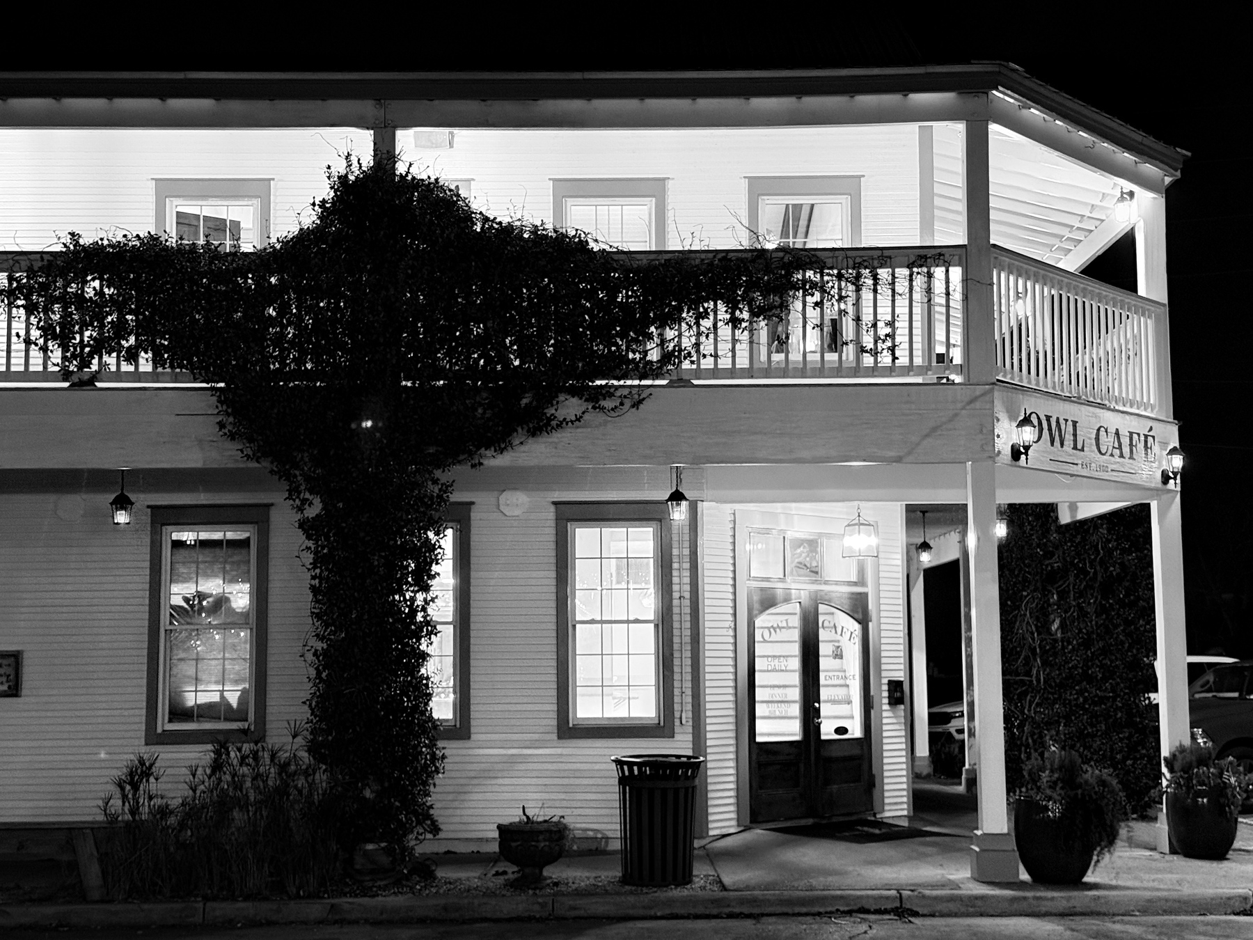 Auto-generated description: A two-story building features the OWL CAFE sign, with ivy climbing its facade and a warmly lit entrance at night.