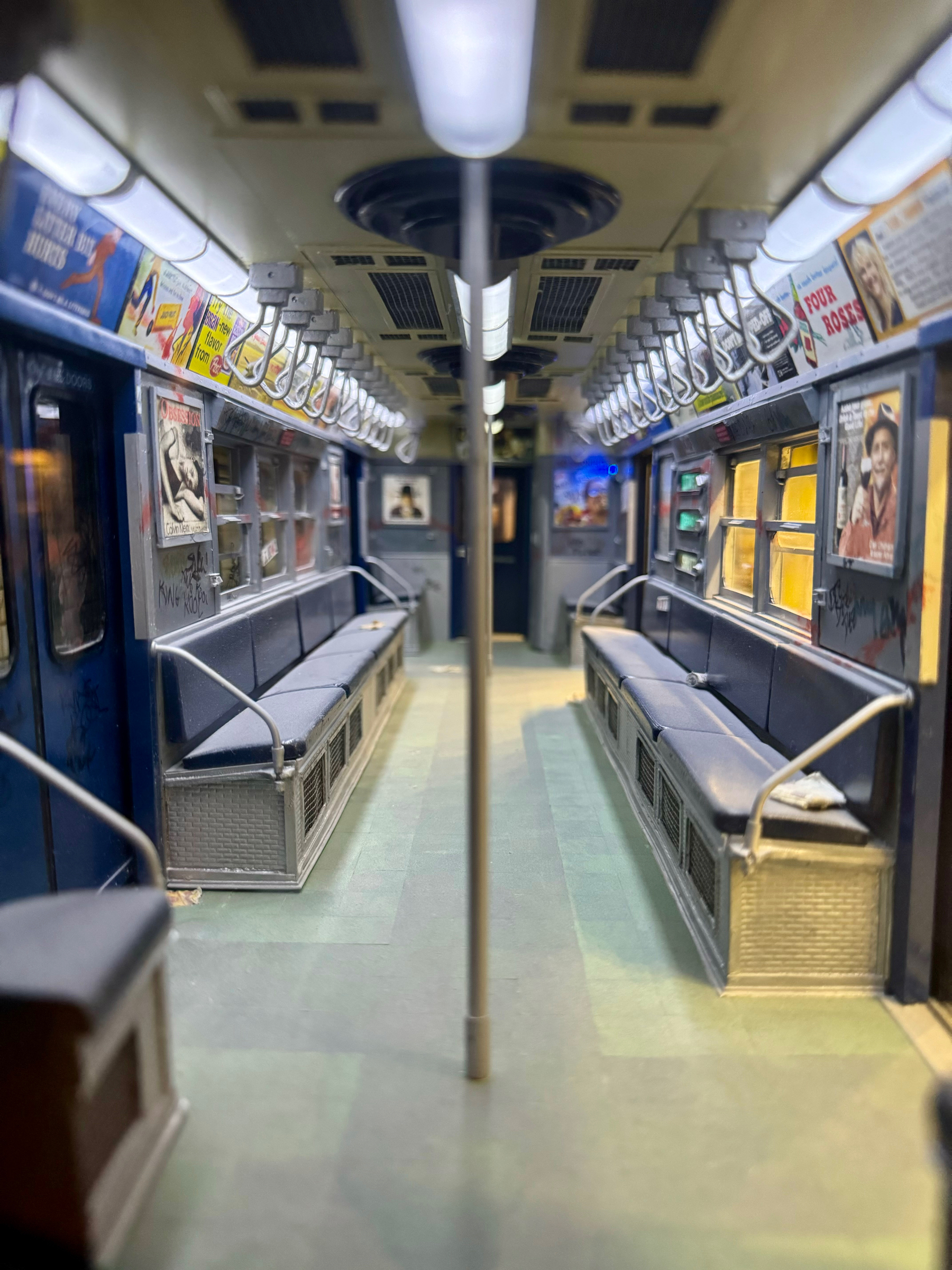 Interior of an empty subway car with benches, handrails, advertisements, and overhead lighting.