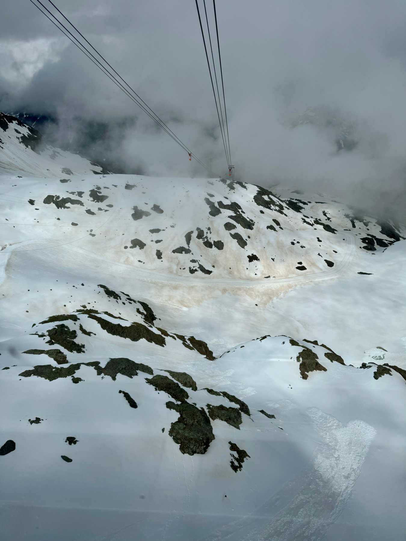 Aerial view of a snowy mountain landscape with cable car lines disappearing into a cloudy sky.