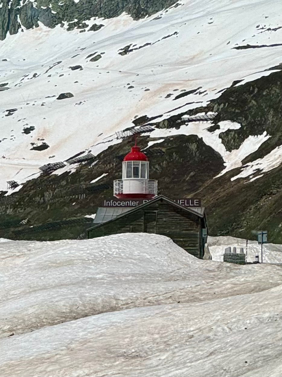 A red-roofed lighthouse-style building labeled “Infocenter” perched on a snow-covered landscape with mountainous terrain in the background.