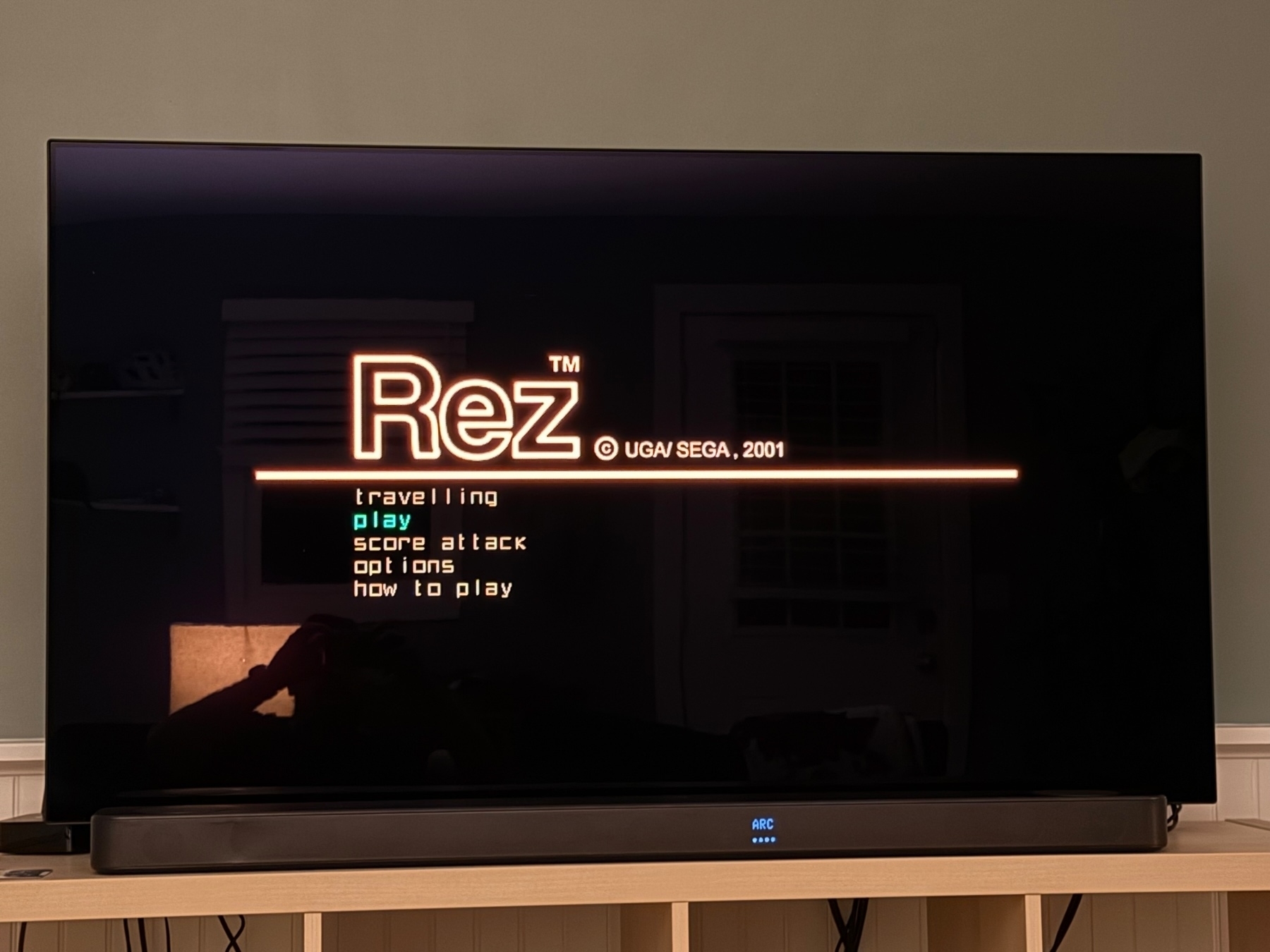 TV screen displaying the game menu for “Rez” by UGA/SEGA, 2001. Options include “travelling,” “play,” “score attack,” “options,” and “how to play.” 