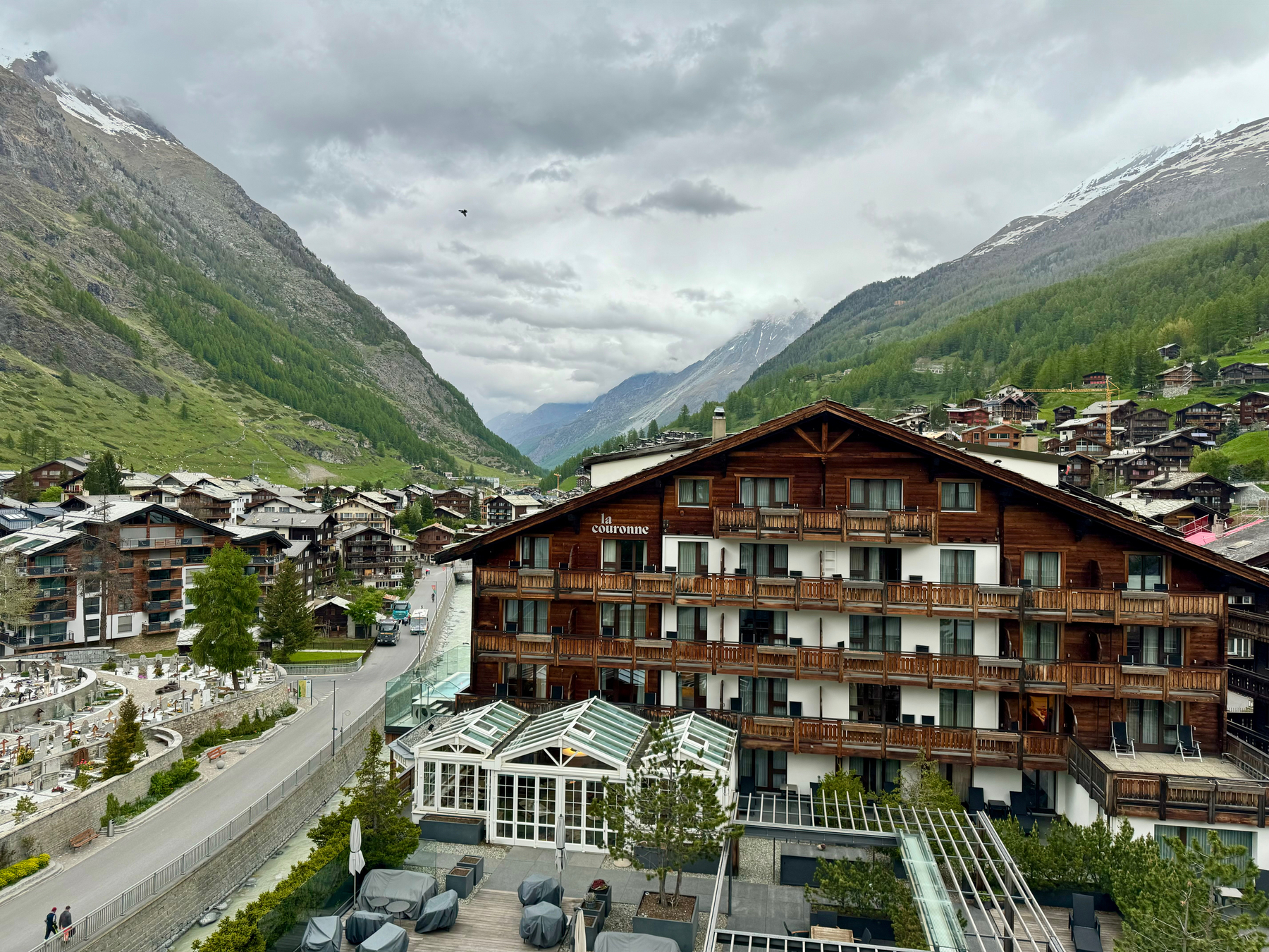 Alpine village with chalet-style buildings nestled between green mountain slopes under a cloudy sky.