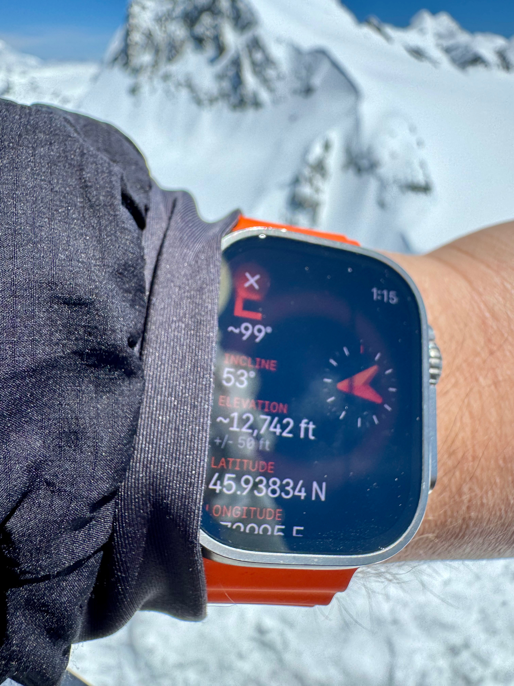 A smartwatch on a wrist displaying the incline, elevation, and GPS coordinates against a snowy mountain backdrop. It shows an elevation of ~12,742 ft. 