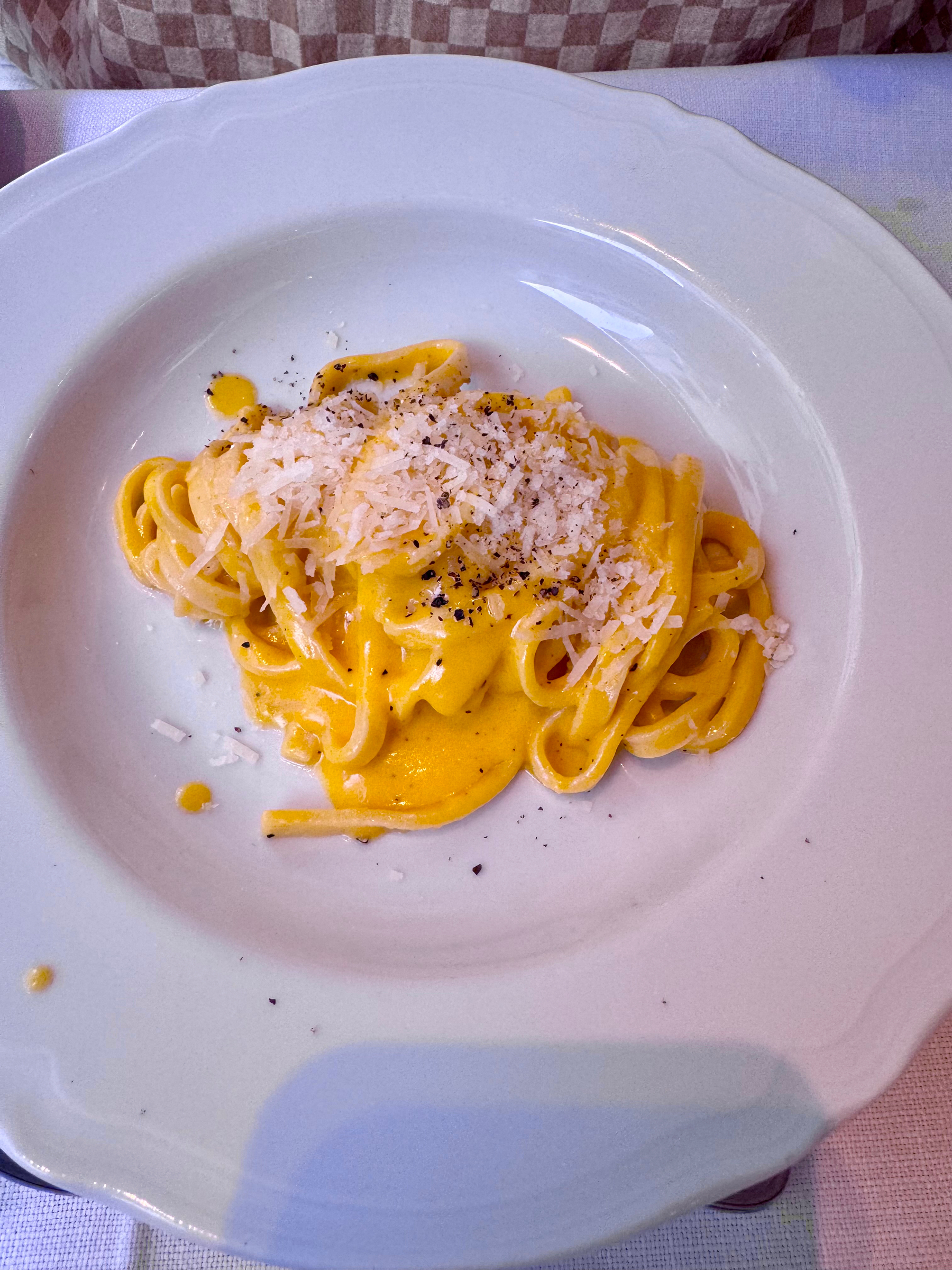 A white plate containing a serving of creamy pasta, likely tagliatelle, topped with grated cheese and a sprinkle of black pepper. The dish is called cachio e burro. 
