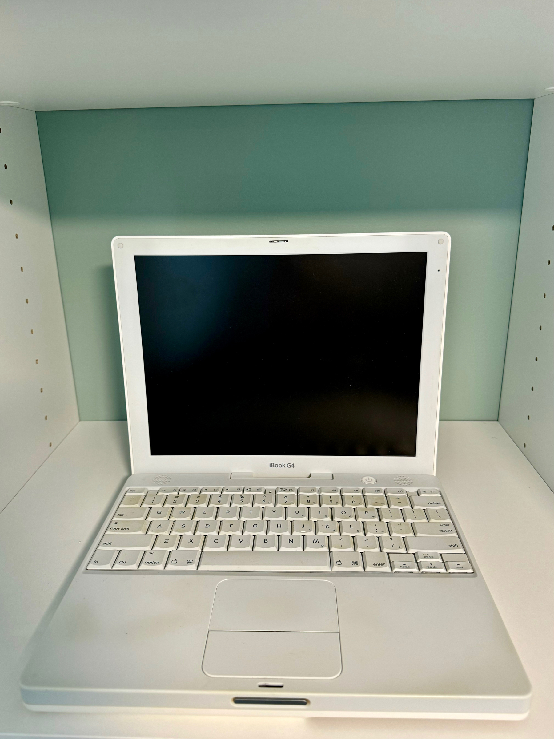 A white iBook G4 laptop, situated on a shelf.