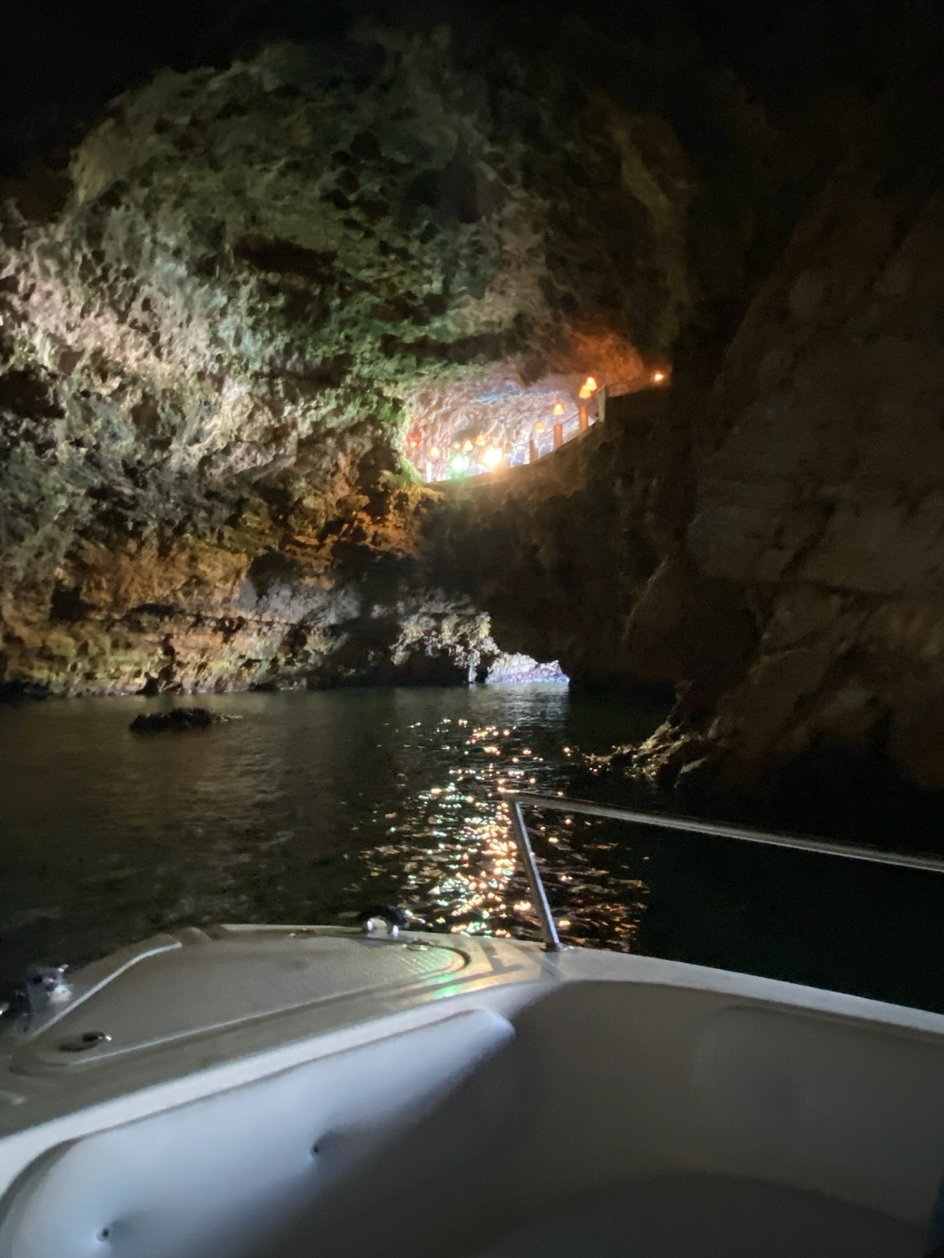 A boat is shown inside a dimly lit cave, with colorful lights illuminating an interior pathway and rocky walls.