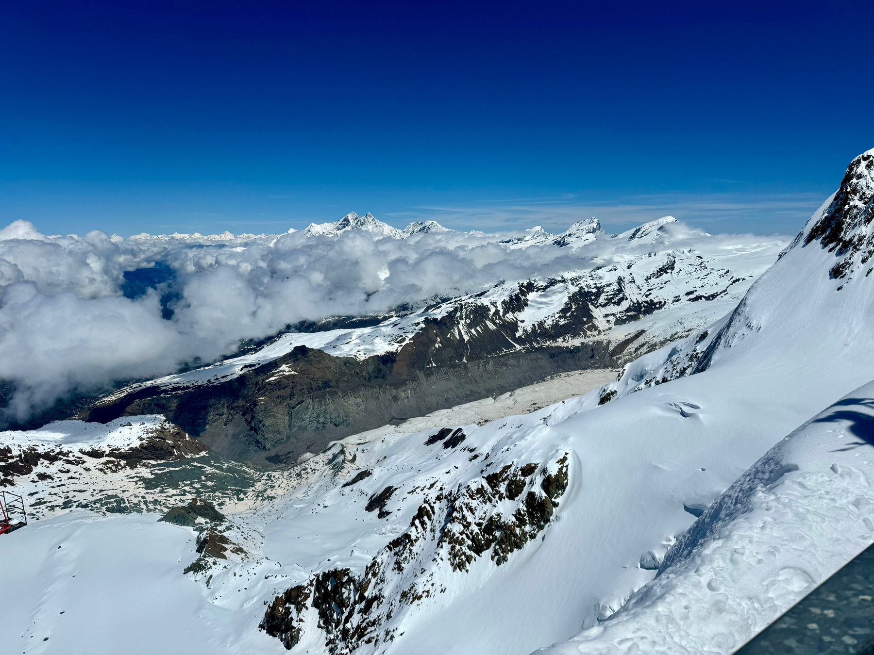Snow-covered mountain peaks with clouds nestled in the valleys, under a clear blue sky.