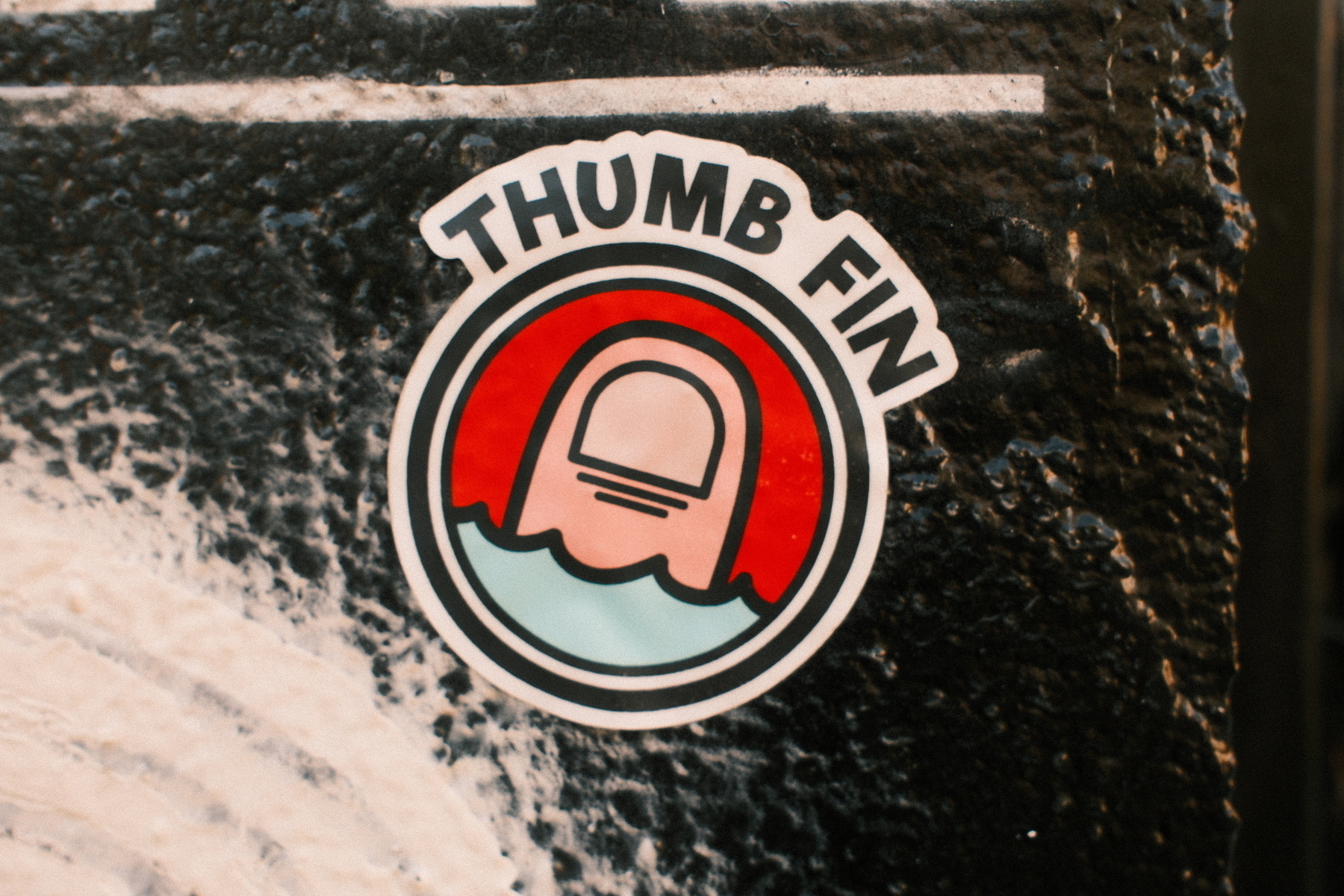 Auto-generated description: A sticker features an image of a thumb-shaped fin in water with the words THUMB FIN above it.